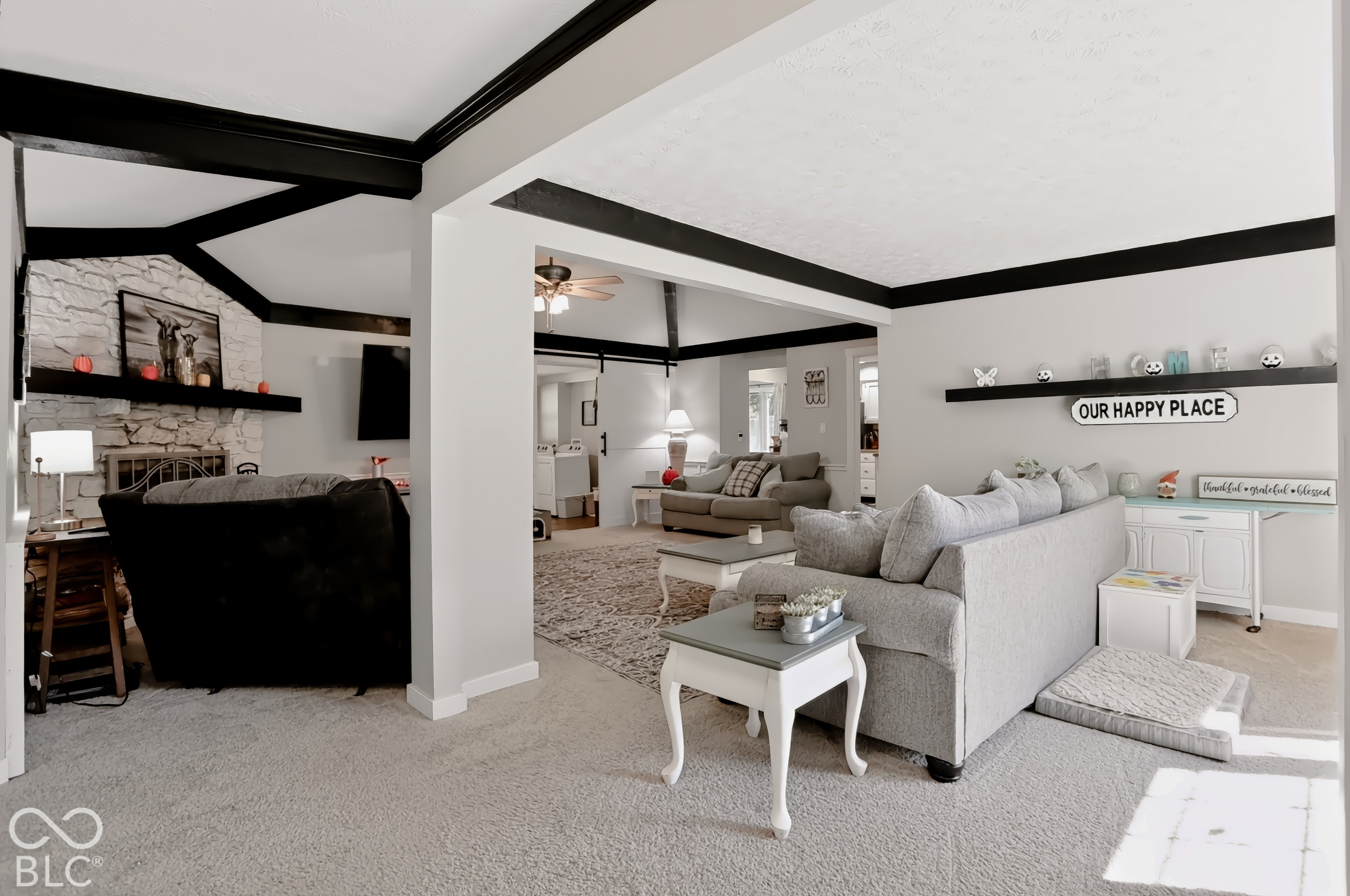 Carpeted living area featuring a stone-clad fireplace with a wood mantel, exposed ceiling beams, and recessed lighting