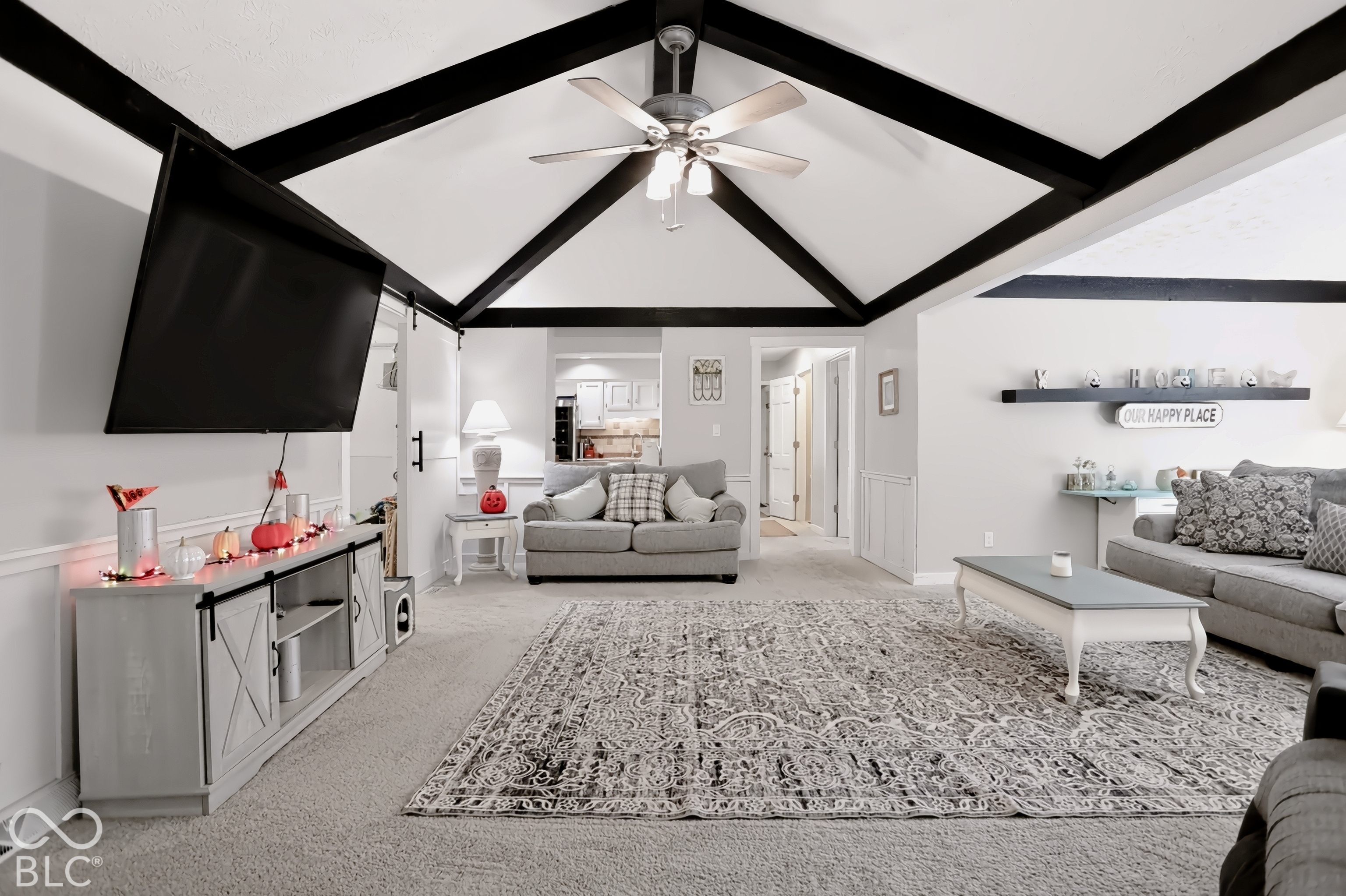 Vaulted ceiling with exposed black beams, ceiling fan, and carpeted flooring