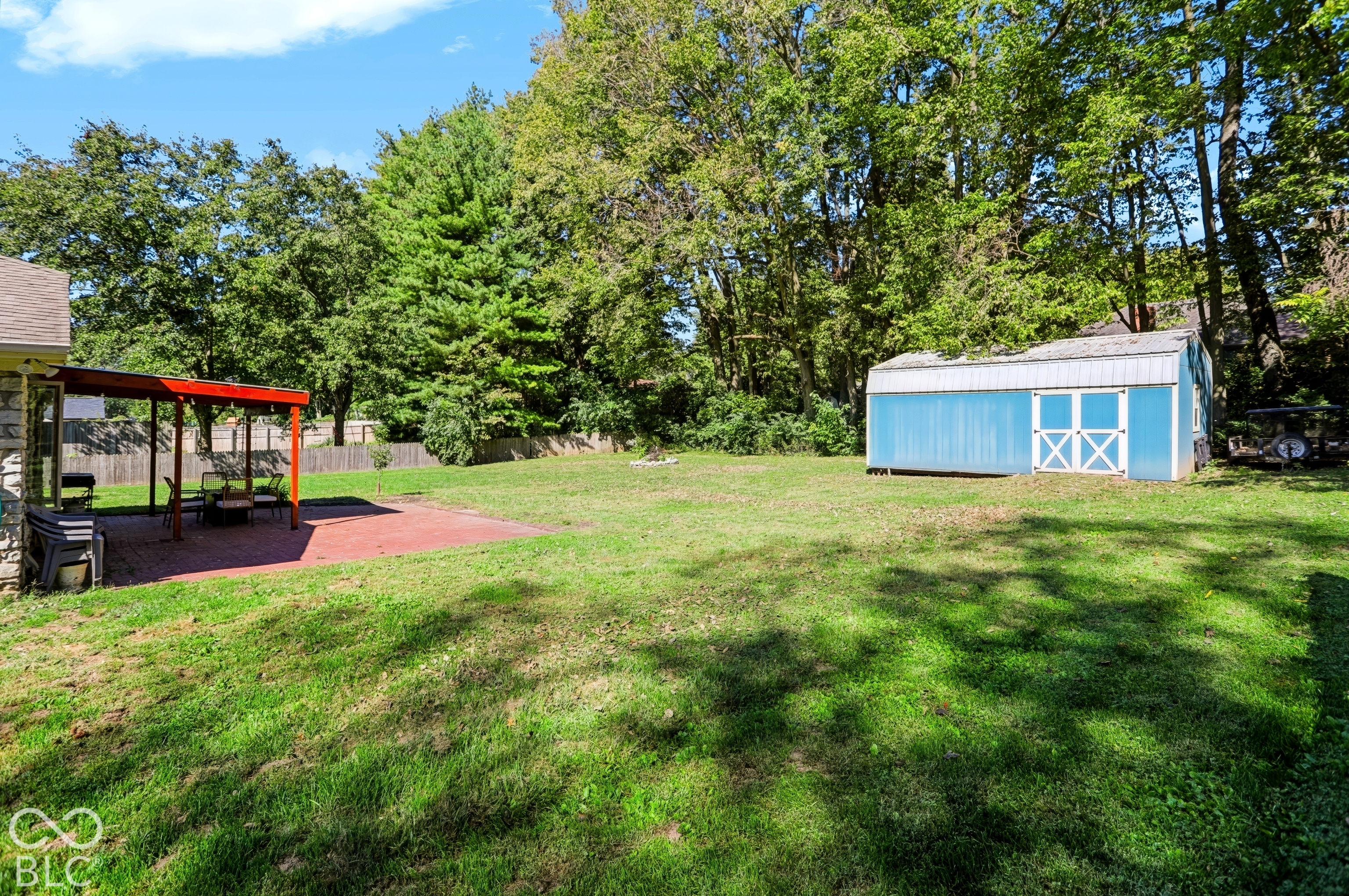 Expansive grassy yard with mature trees, red-framed patio cover, and a detached storage shed