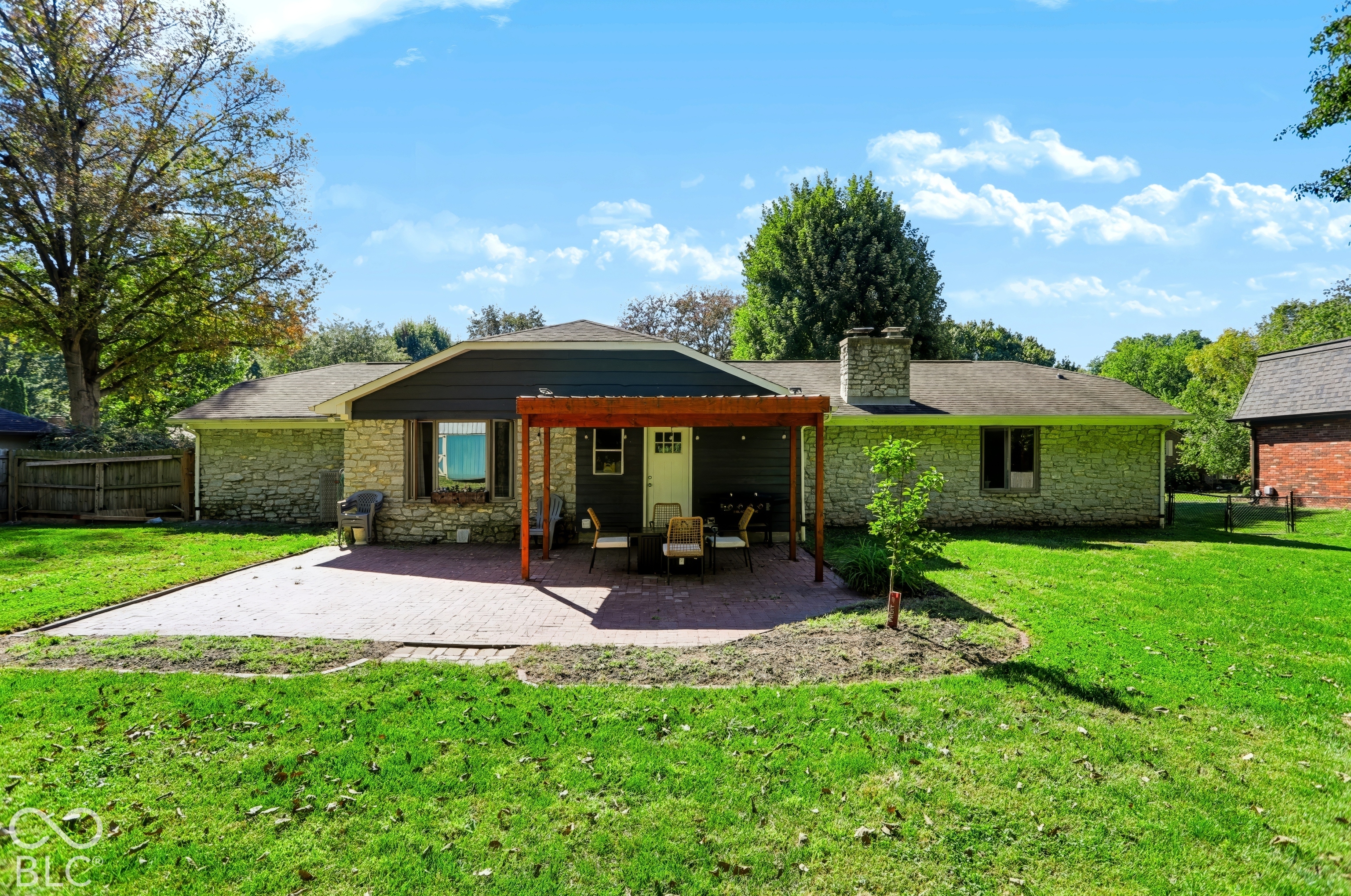 Expansive backyard with a large paver patio, wood pergola, and stone exterior