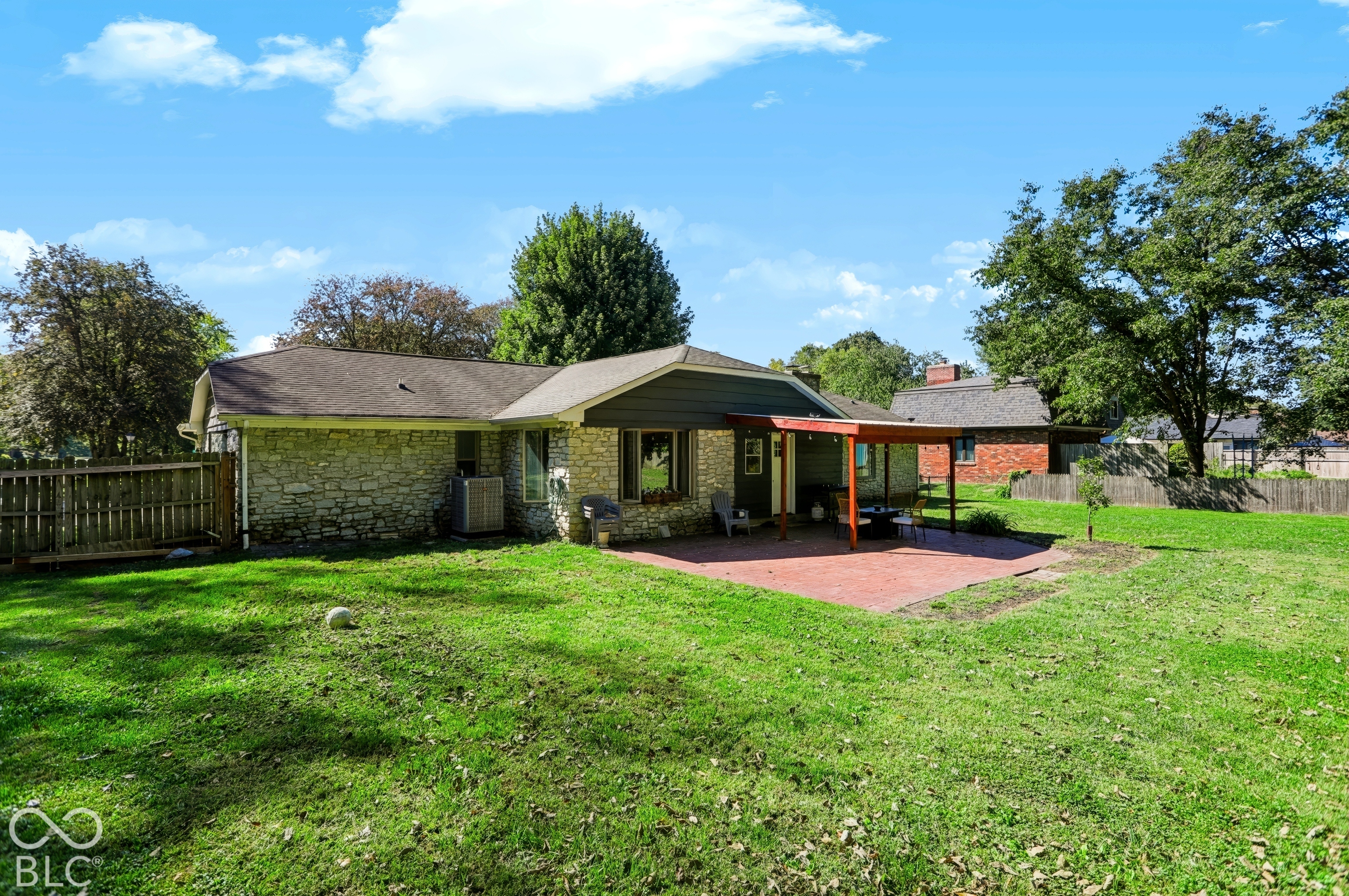 Expansive backyard with a manicured lawn, brick patio, covered outdoor living area, and stone exterior