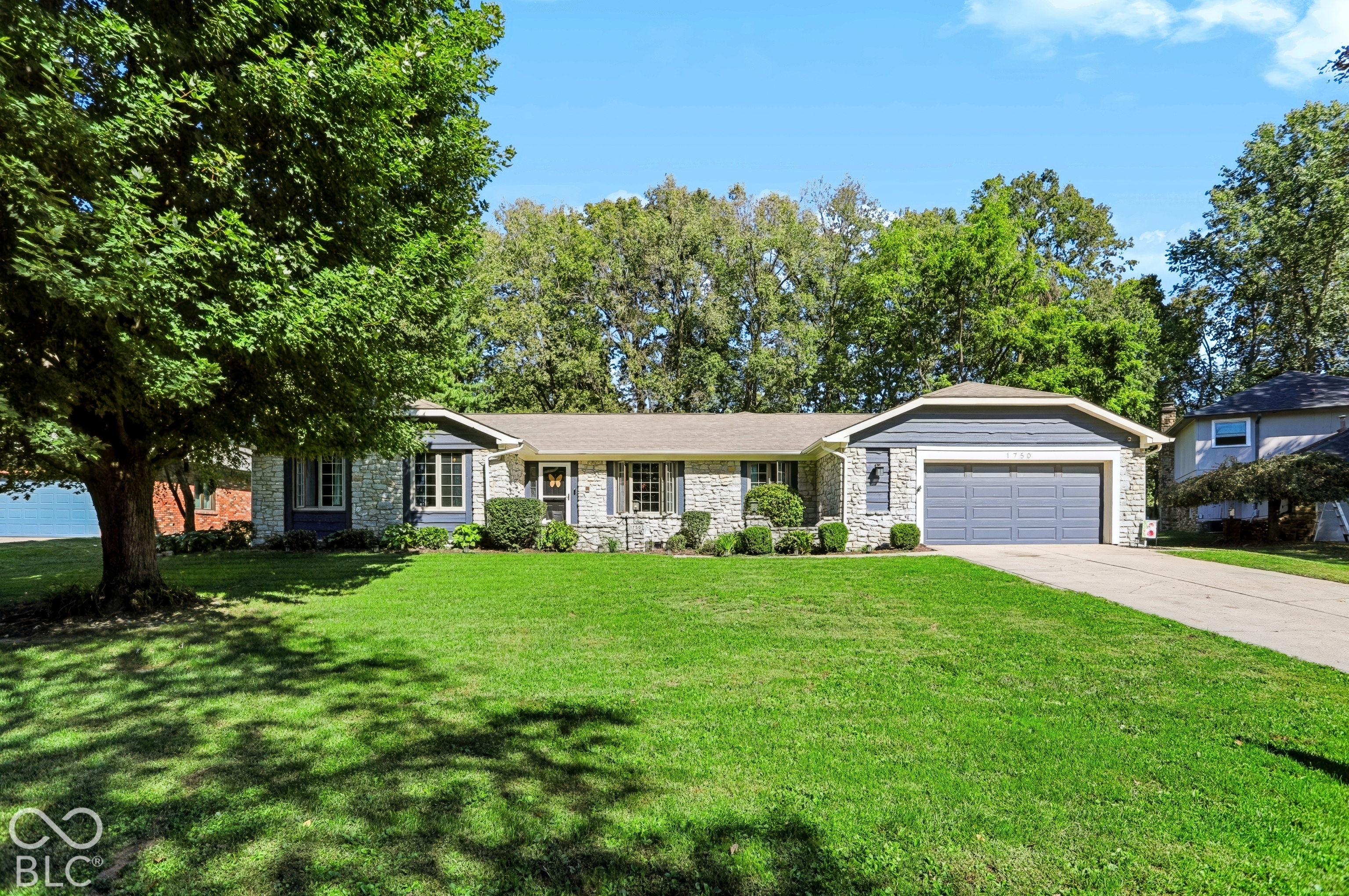 Stone and siding exterior with a two-car garage, mature trees, and a concrete driveway