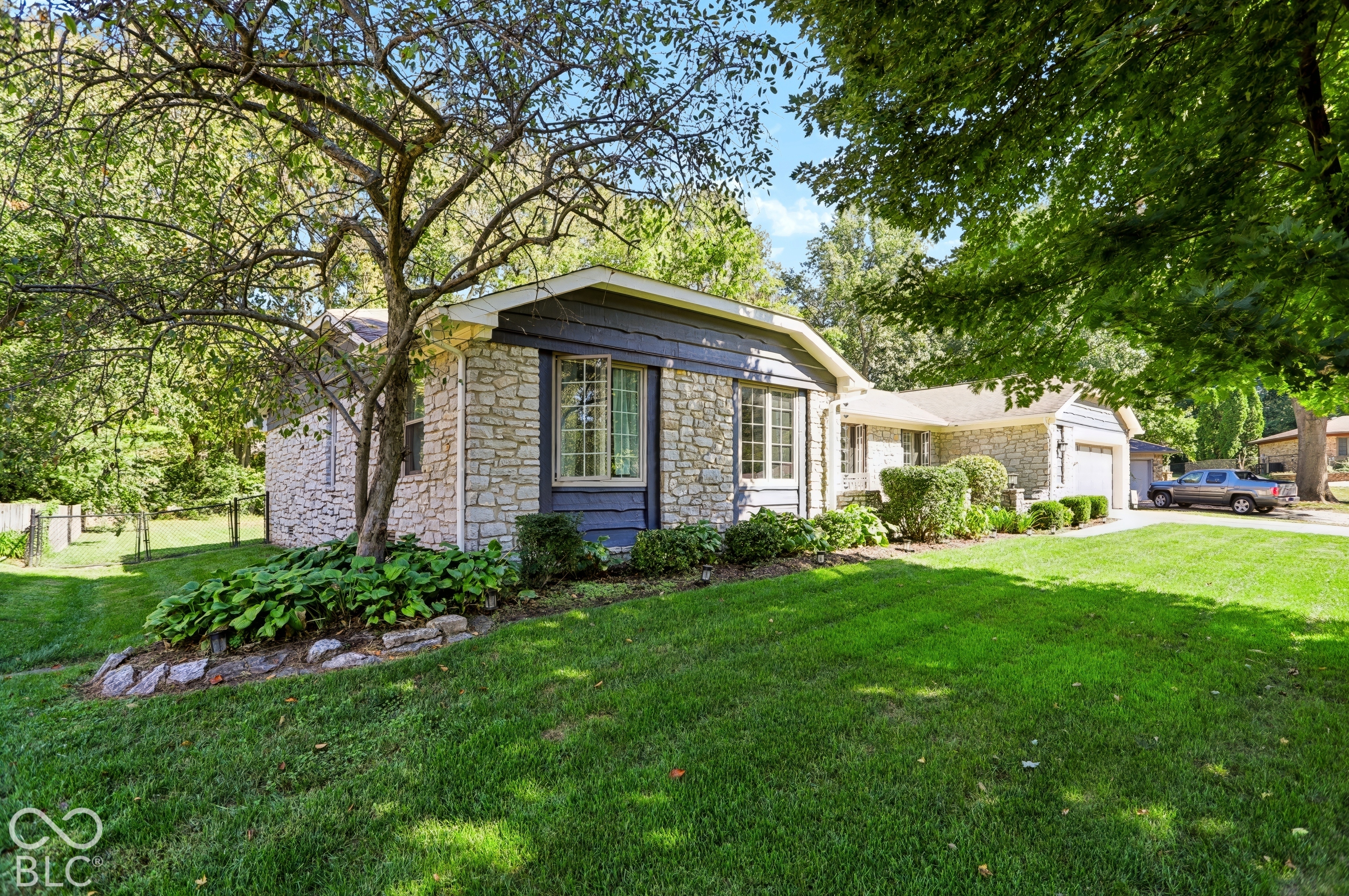 Stone veneer exterior with blue siding accents, bay window, landscaped front yard, mature trees, and an attached two-car garage