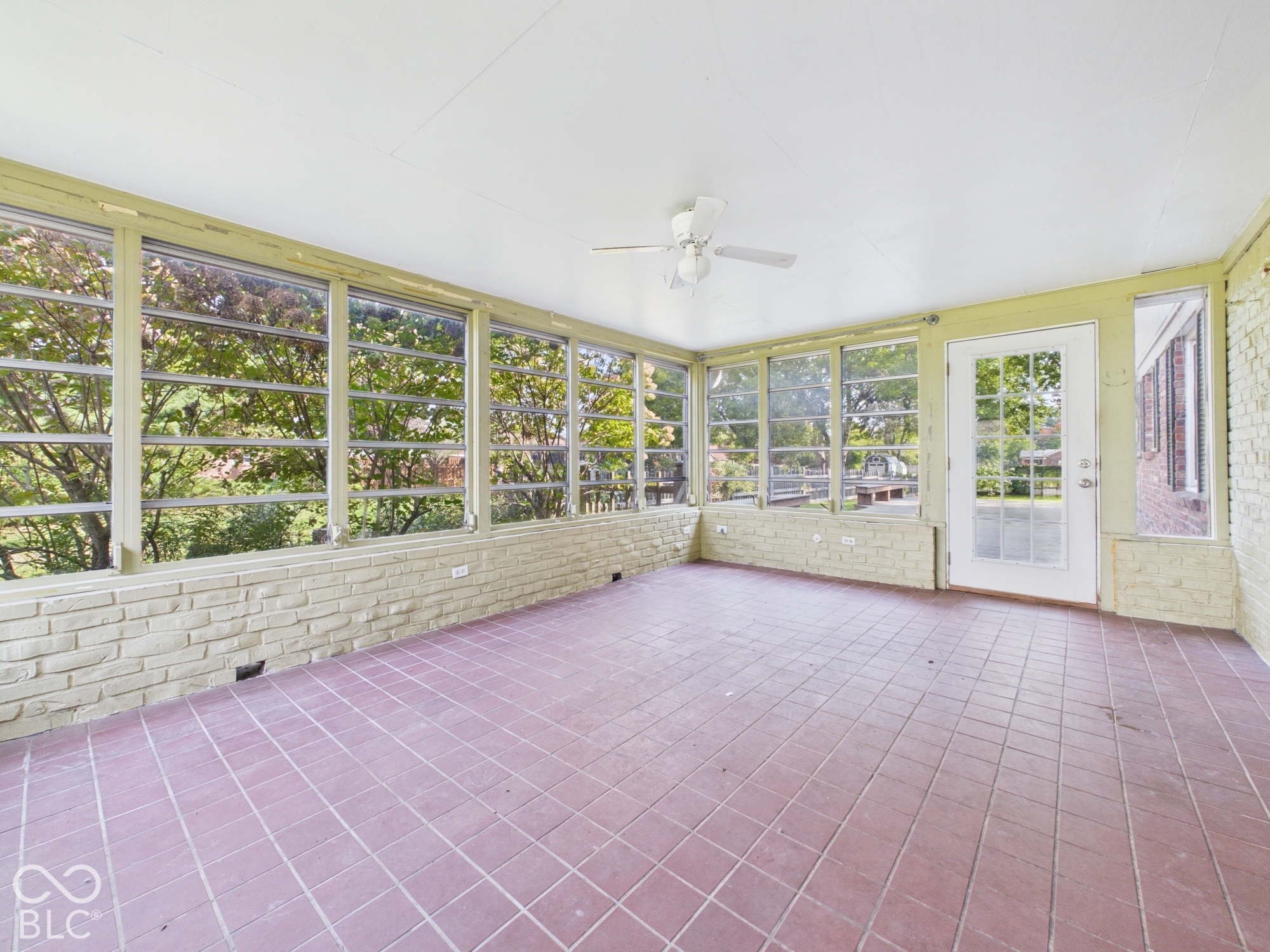 Expansive screened porch with a durable tile floor, a ceiling fan, and a brick knee wall