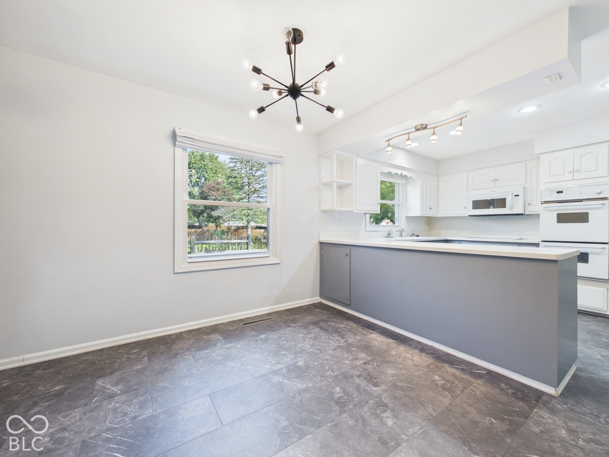 White kitchen cabinetry with integrated double ovens and microwave, complemented by a gray island with a light-colored countertop