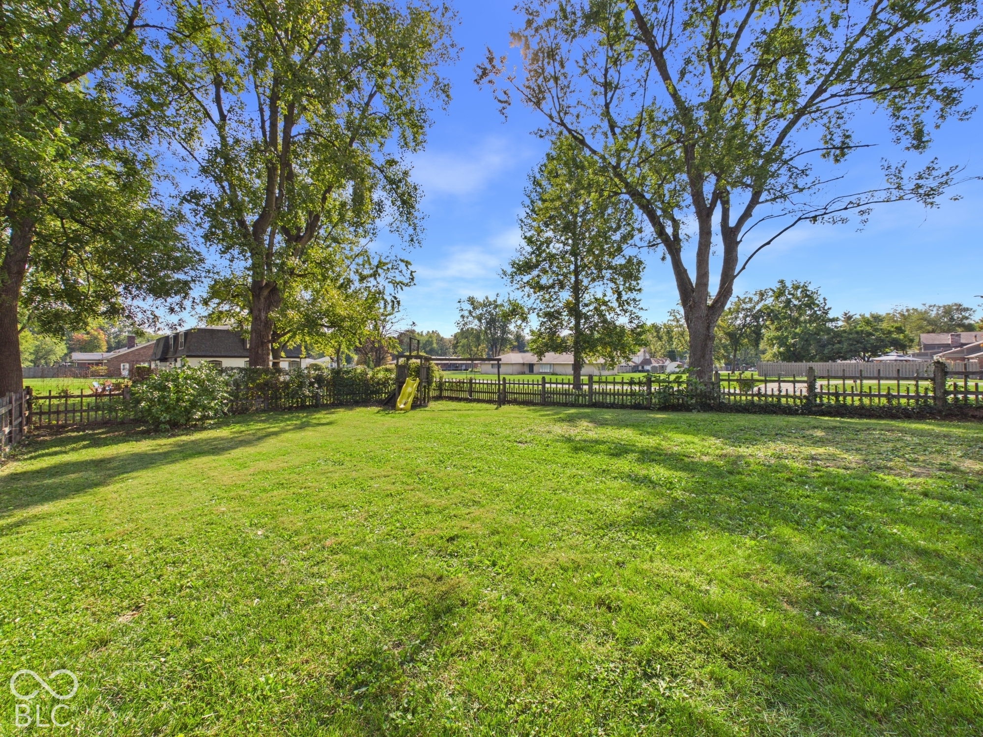 Expansive lawn area featuring mature trees and a wooden picket fence