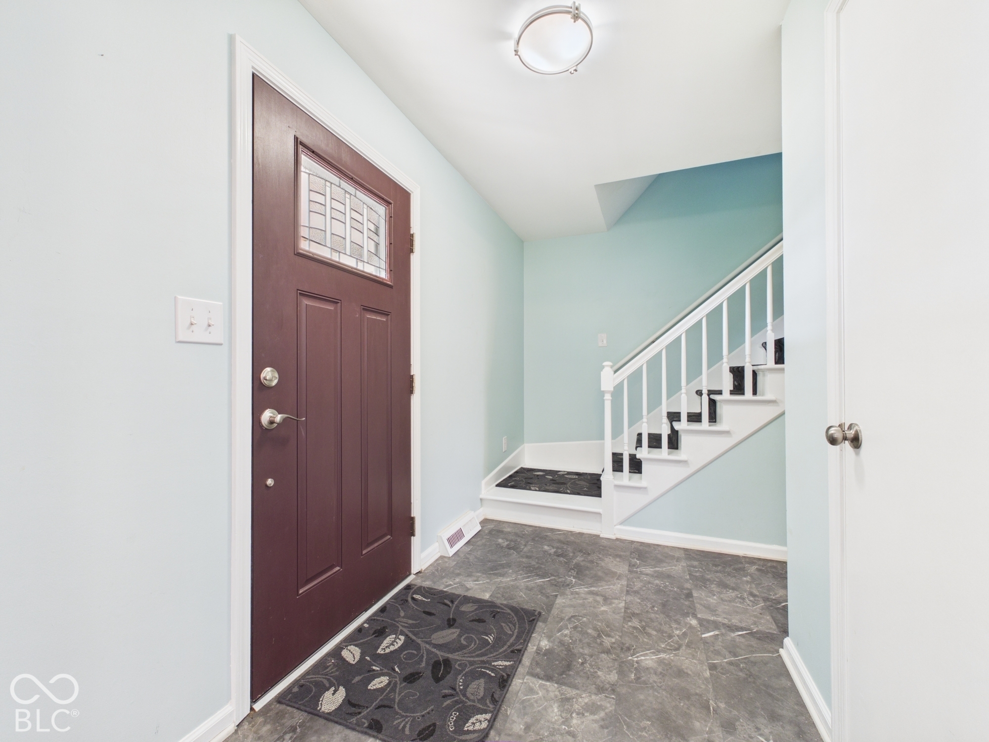 Entryway featuring a decorative transom door, durable tile flooring, and a staircase with white spindles