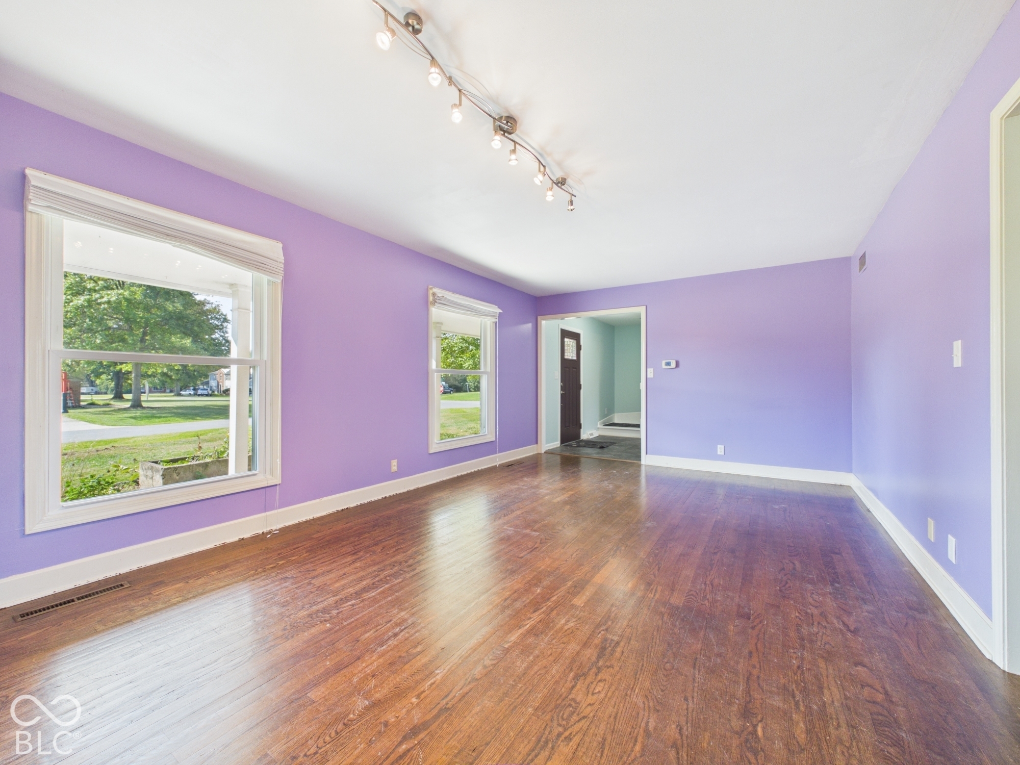 Spacious room featuring wood-finish flooring, multiple windows, and a track lighting fixture