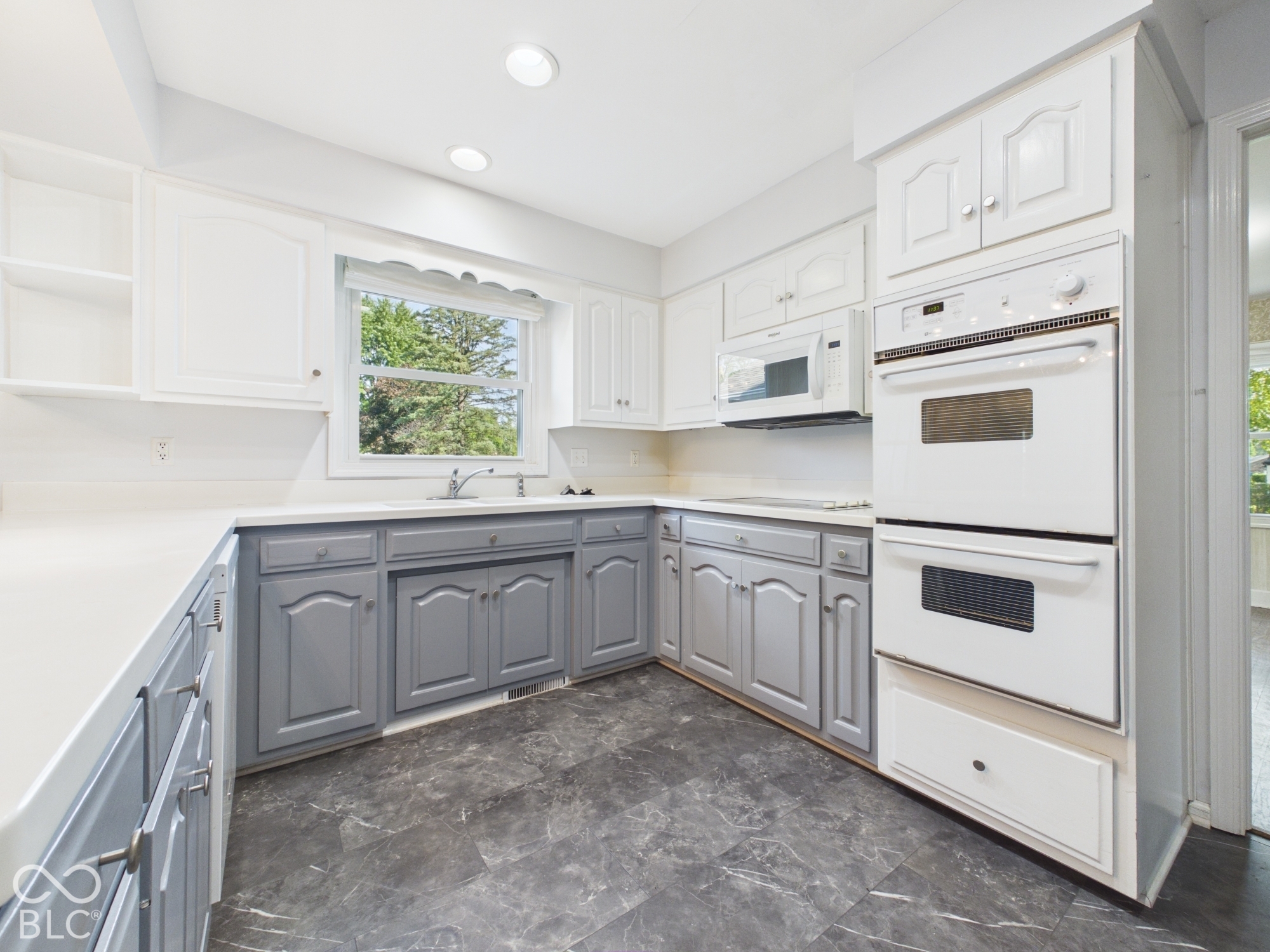 Kitchen featuring two-tone cabinetry, light-toned countertops, a stainless steel sink, built-in double ovens, and recessed lighting