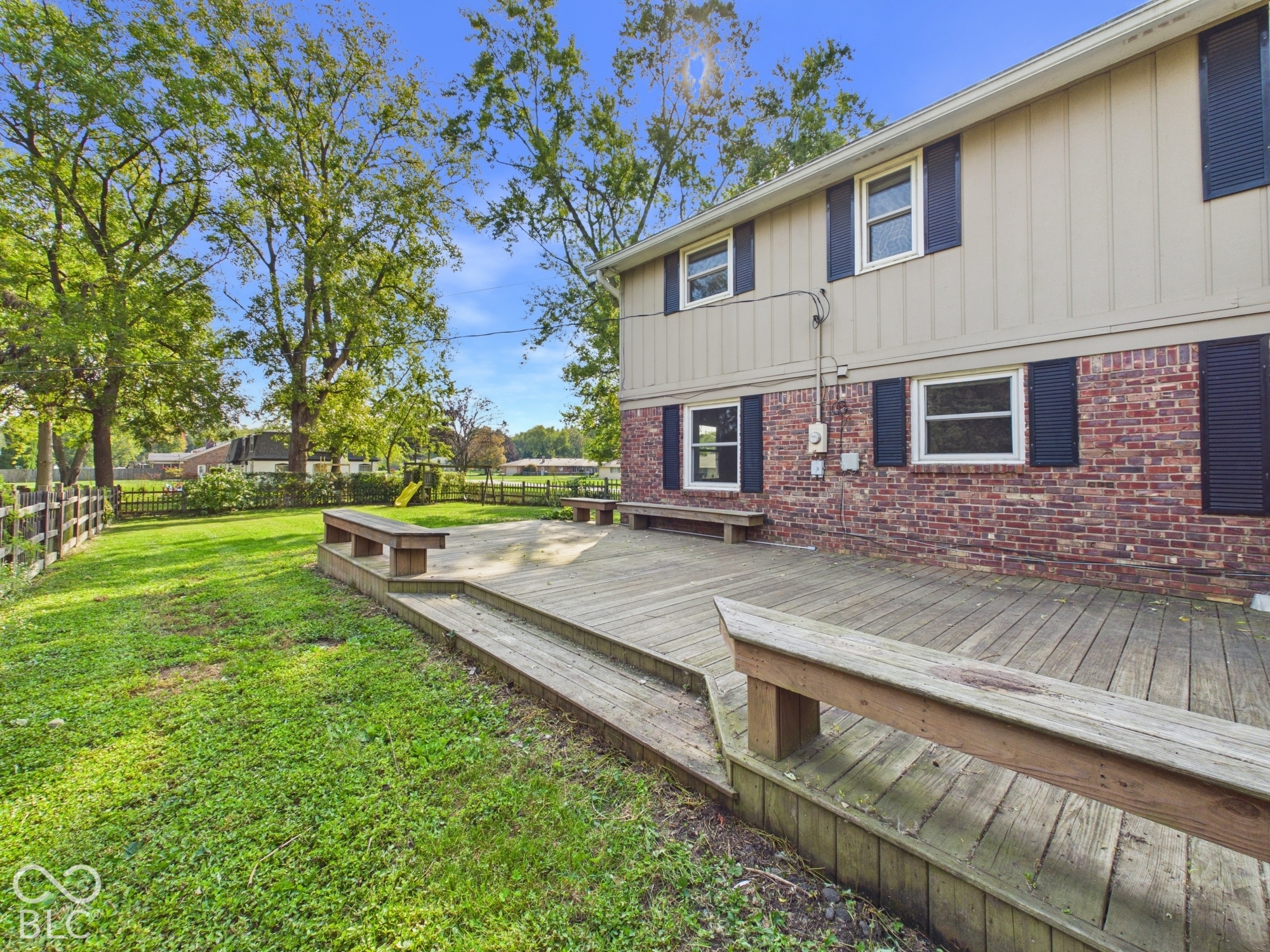 Expansive backyard featuring a multi-level wooden deck with integrated benches, a manicured lawn, and mature trees