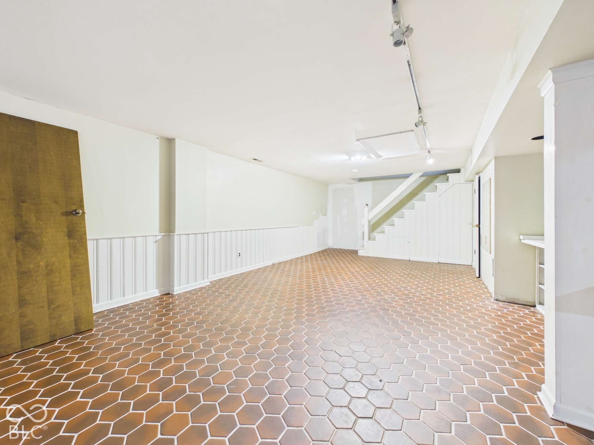 Spacious room featuring hexagonal floor tiles, white wainscoting, and track lighting