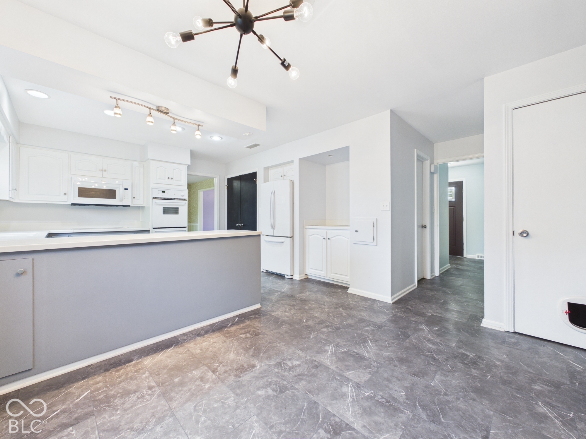 Modern kitchen featuring white cabinetry, integrated appliances, a spacious central island, and contemporary overhead lighting