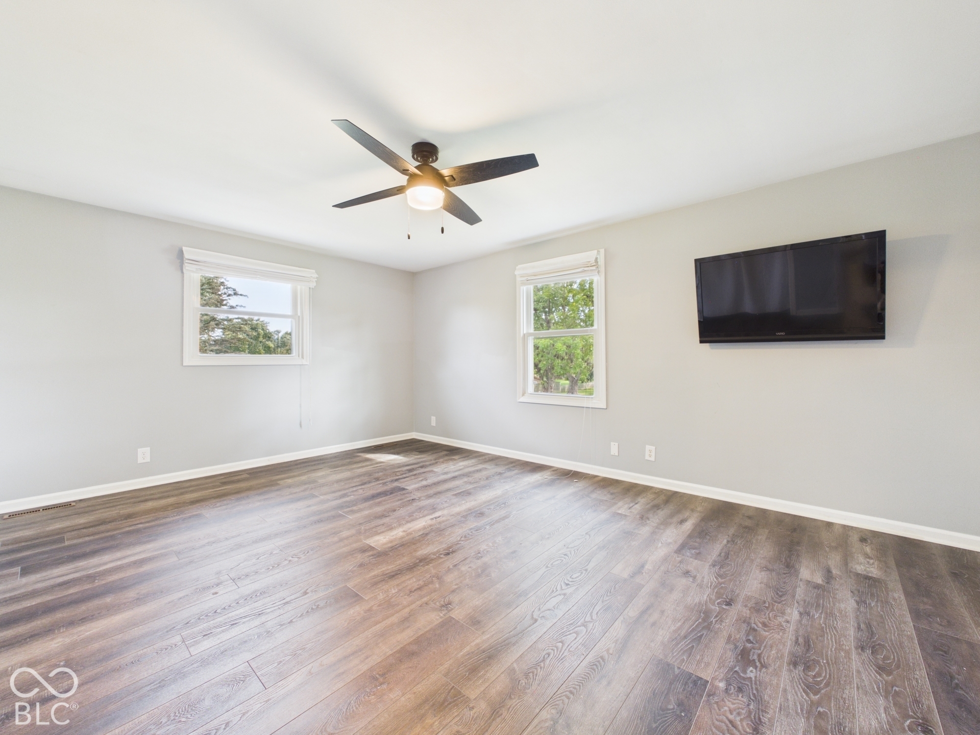 Wood-finish flooring, two windows with blinds, ceiling fan with integrated lighting, and light-toned wall paint