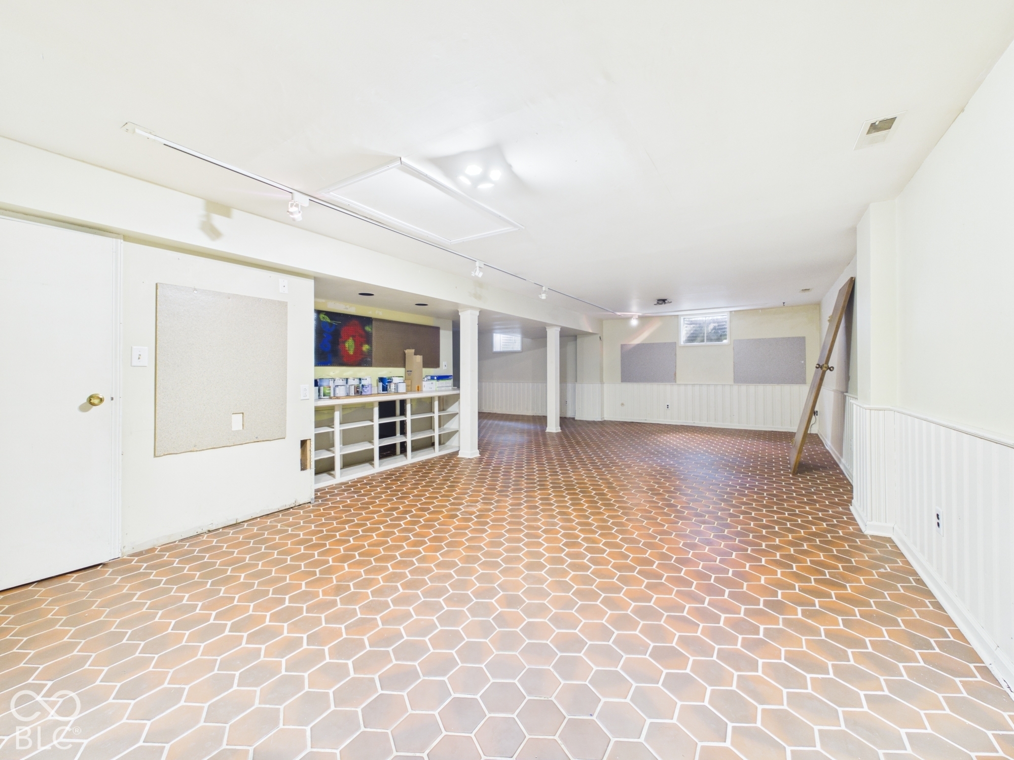 Spacious room featuring hexagonal tile flooring, track lighting, built-in shelving, white paneled wainscoting, and recessed windows