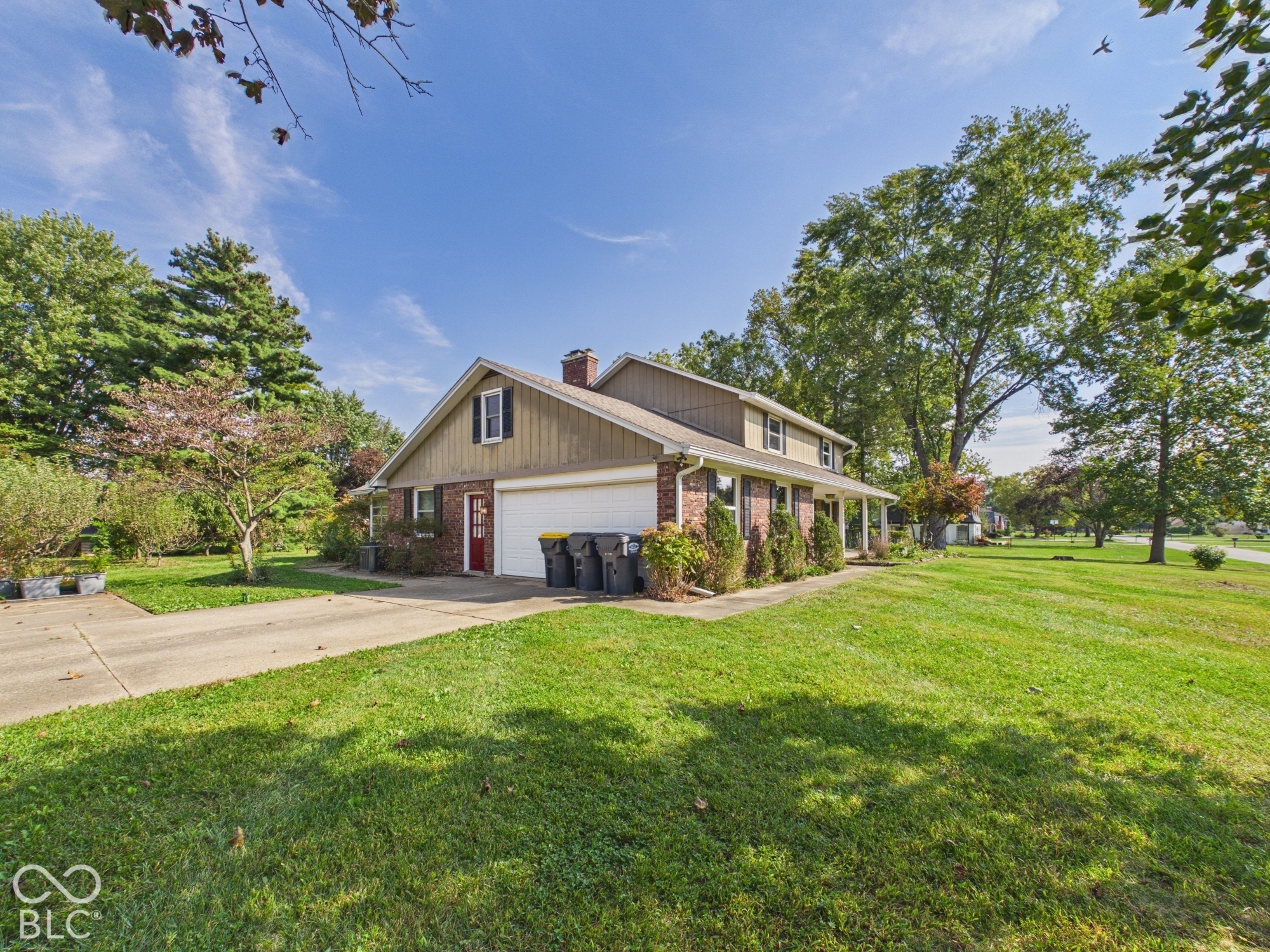 Brick and siding exterior with a white garage door, concrete driveway, and mature landscaping