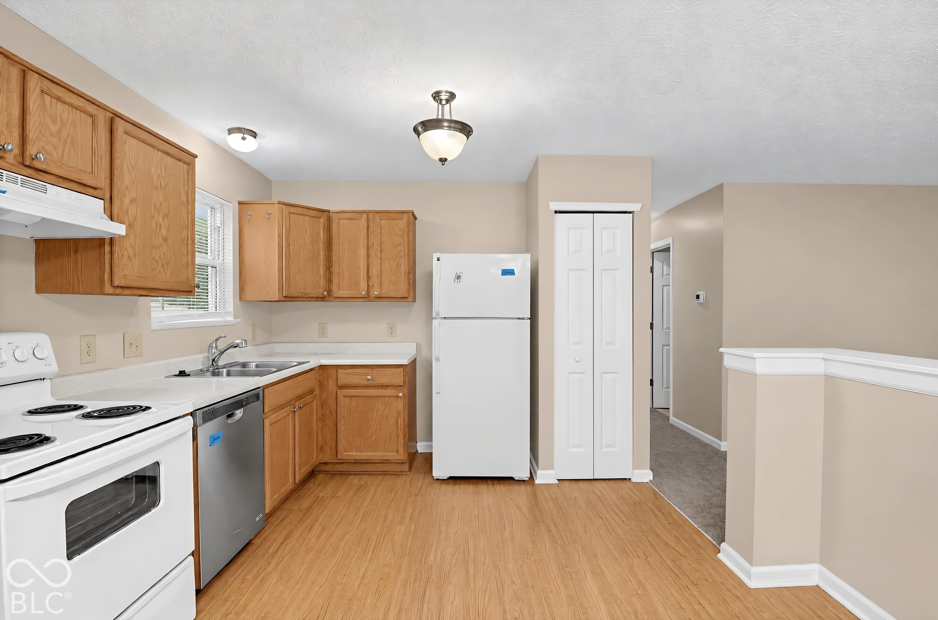 Kitchen featuring natural wood-finish cabinetry, solid-surface countertops, stainless steel dishwasher, and wood-finish flooring