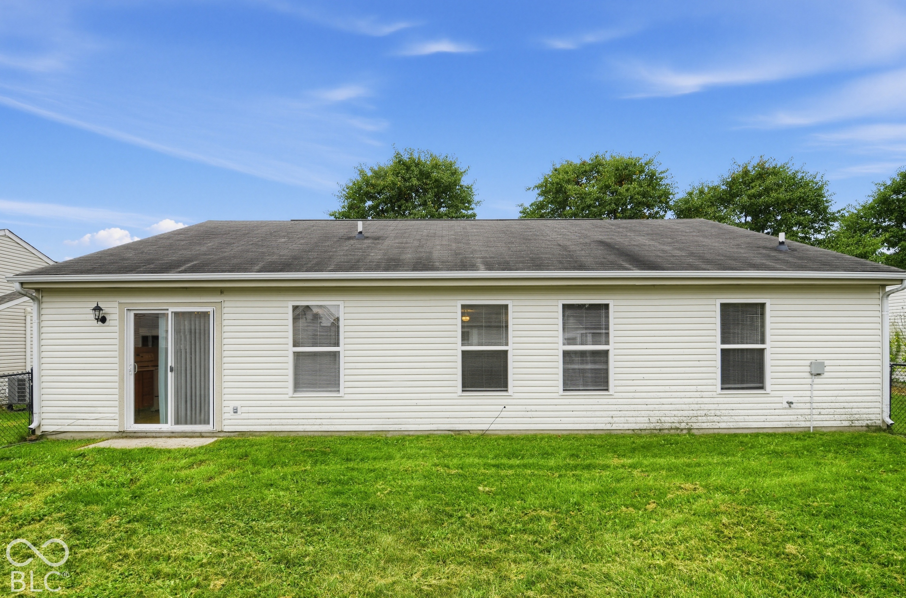 Horizontal vinyl siding exterior featuring a multi-paneled sliding glass door, four rectangular windows, and a paved concrete patio slab