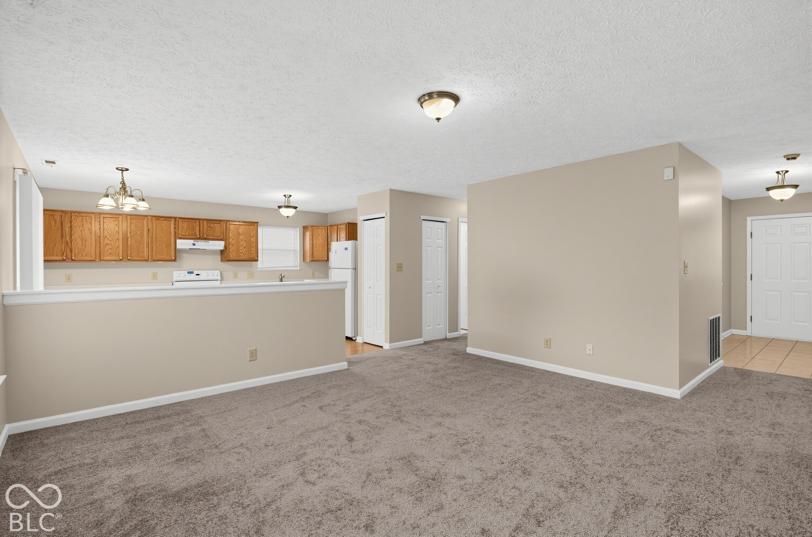 Open-concept interior featuring wood cabinetry, wall-to-wall carpeting, tile flooring, and multiple ceiling-mounted light fixtures