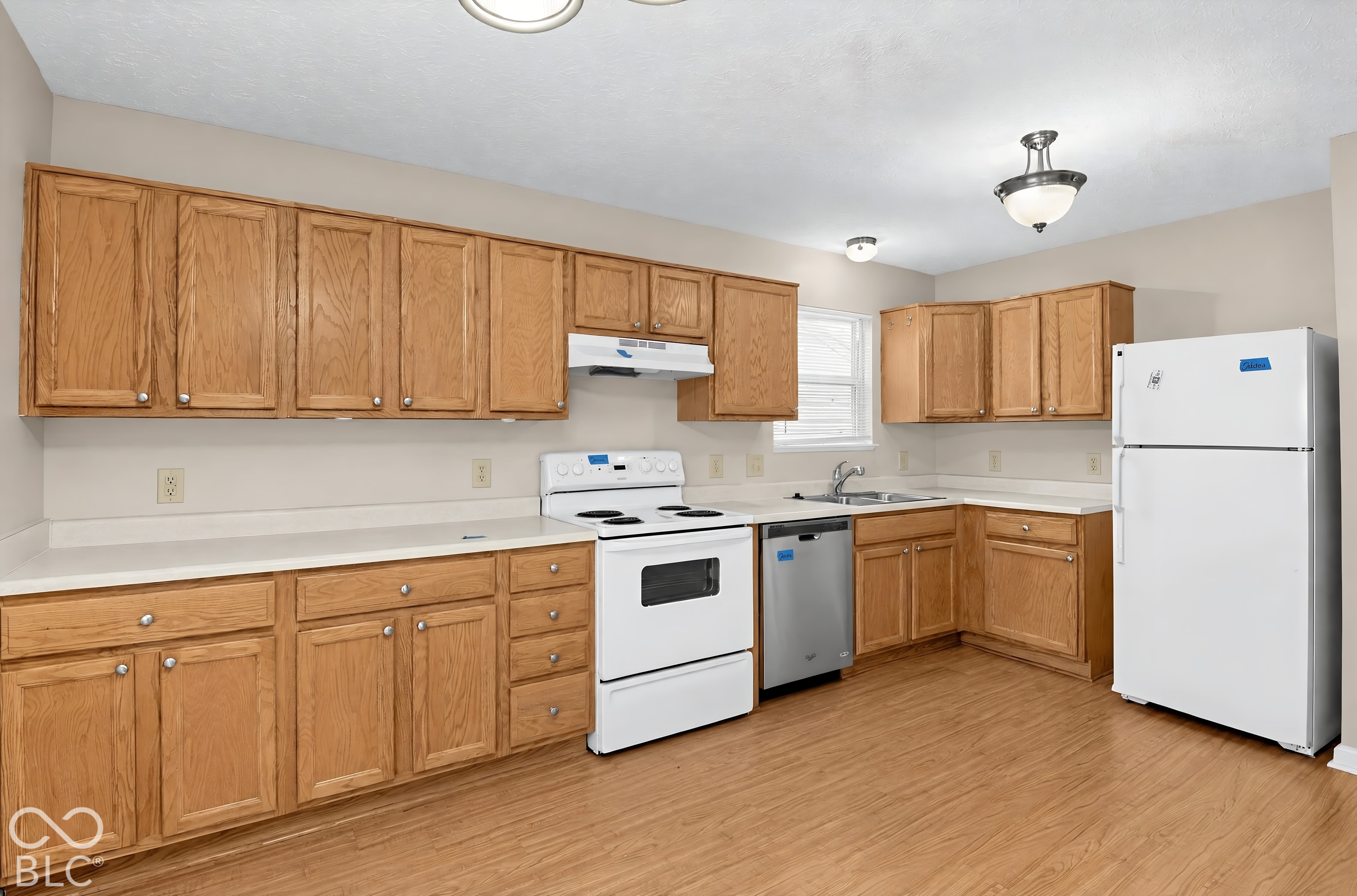 Kitchen featuring wood cabinetry, white solid-surface countertops, wood-finish flooring, and built-in appliances including a range, dishwasher, and refrigerator