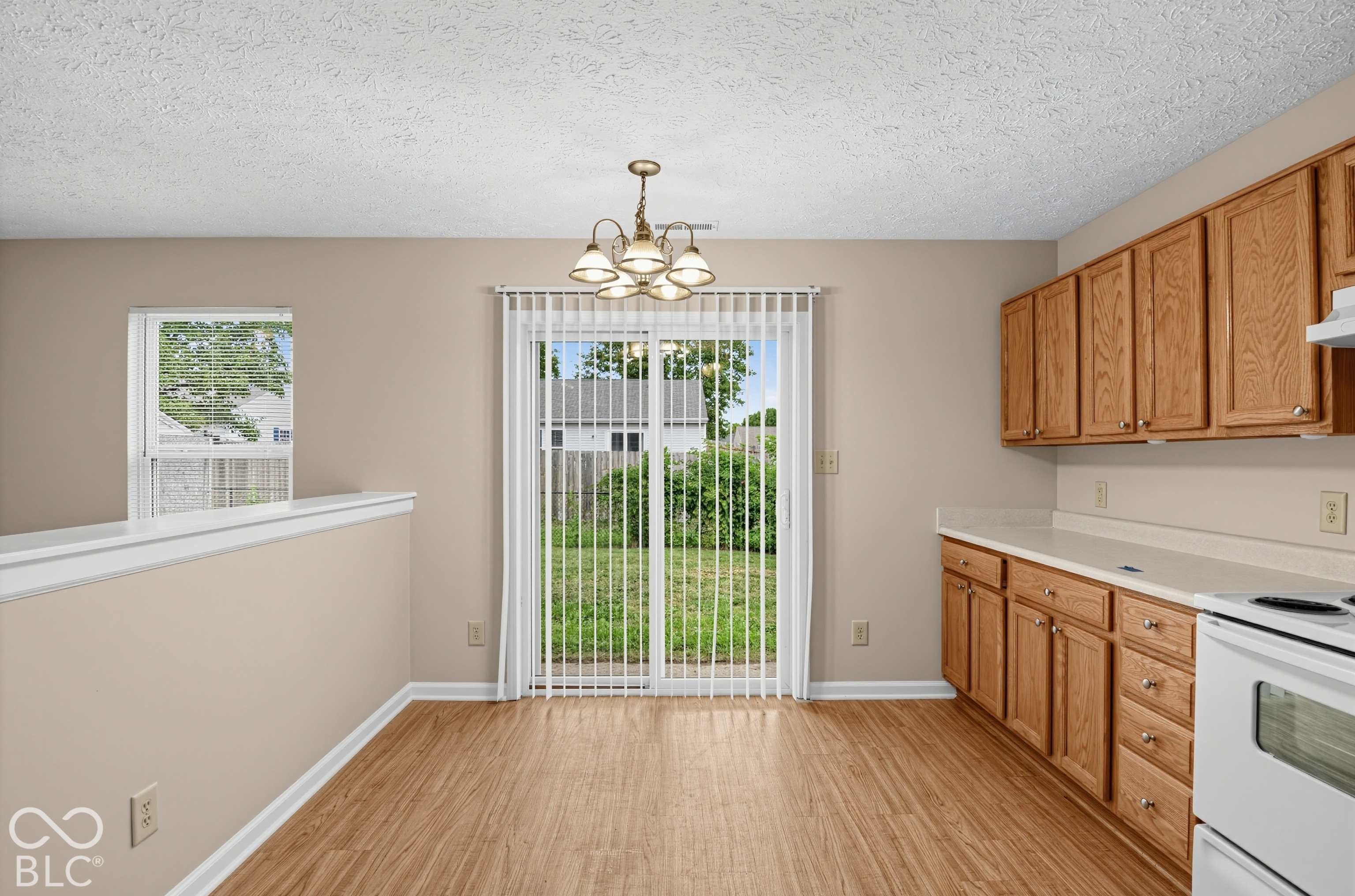 Wood-finish flooring, oak cabinetry, solid-surface countertops, and sliding glass door with vertical blinds