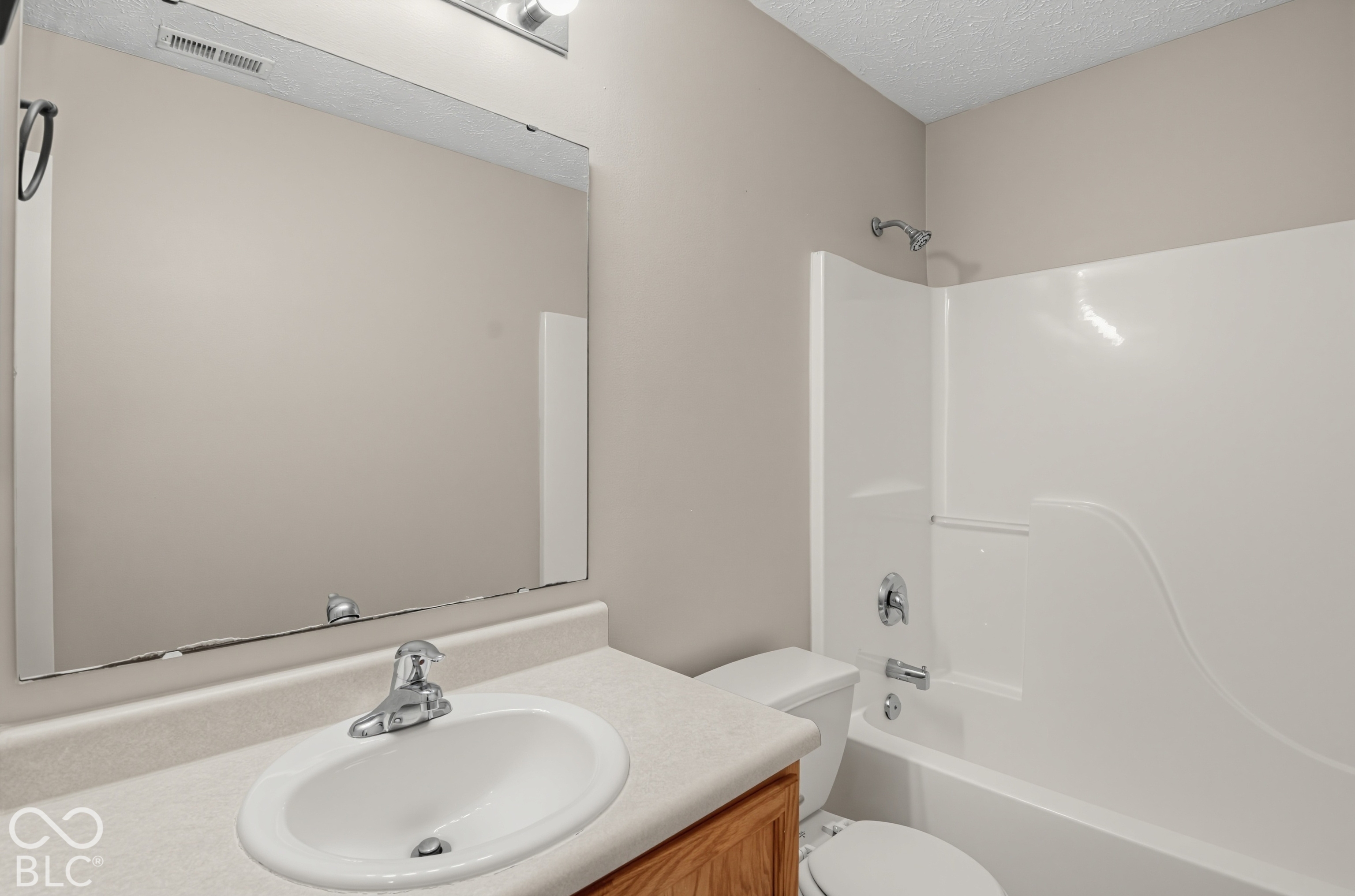Bathroom featuring a wood-finish vanity, integrated countertop with an oval basin, large wall-mounted mirror, and a full-size acrylic tub and shower combination