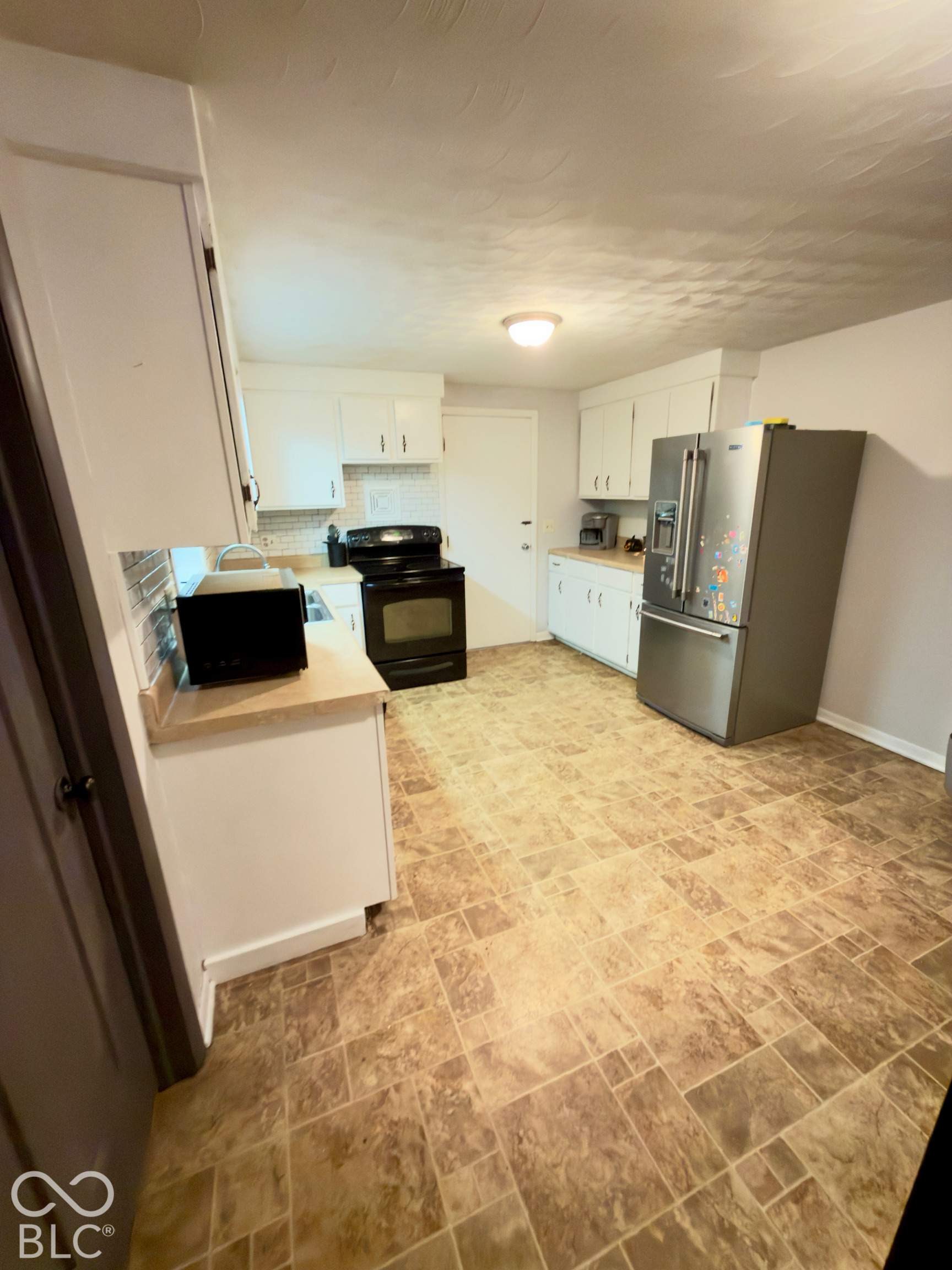 Kitchen featuring white cabinetry, solid-surface countertops, tile backsplash, stainless steel refrigerator, and tiled flooring