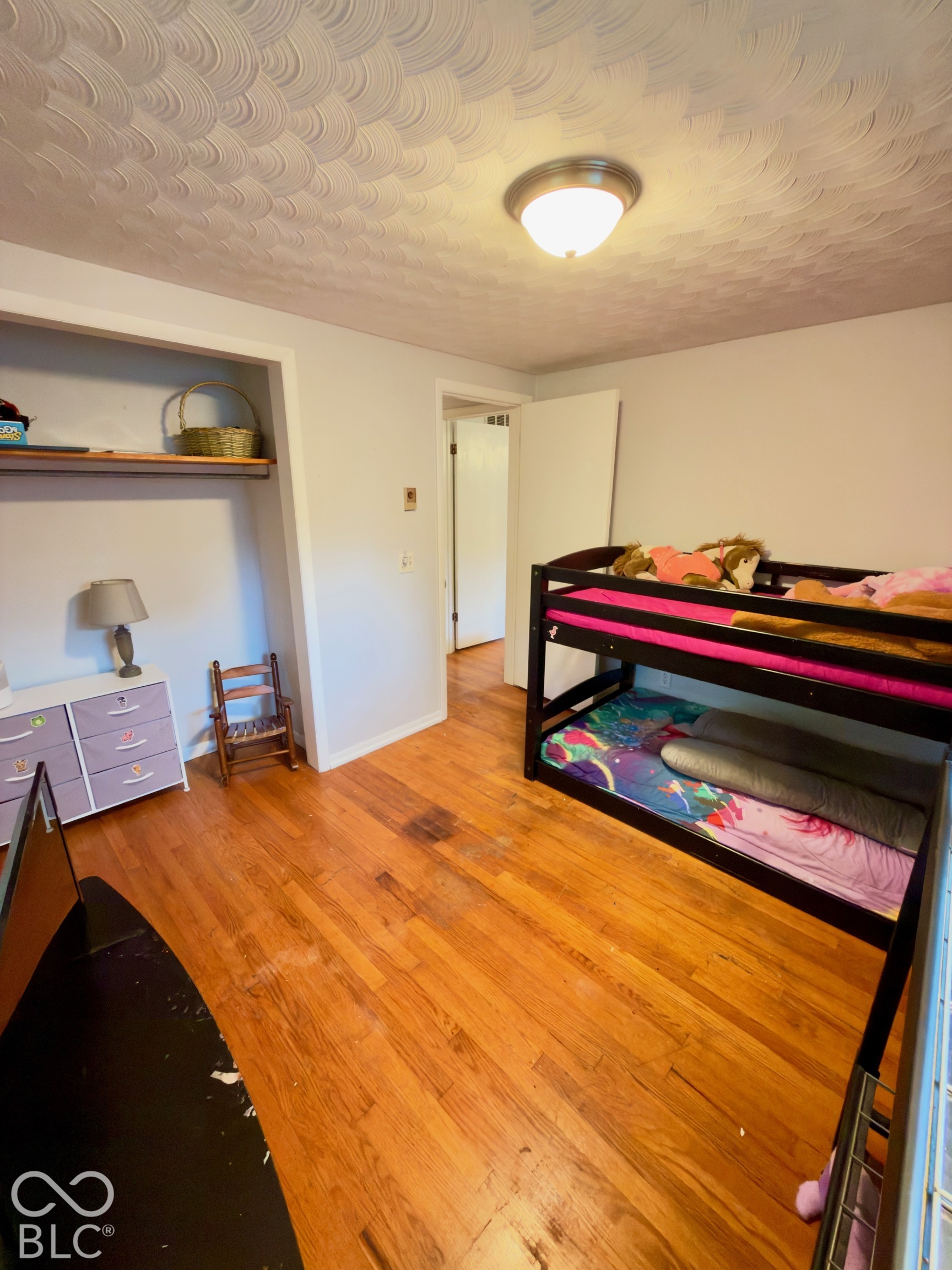 Room featuring wood-finish flooring, a scalloped-pattern ceiling, and a built-in recessed closet shelf