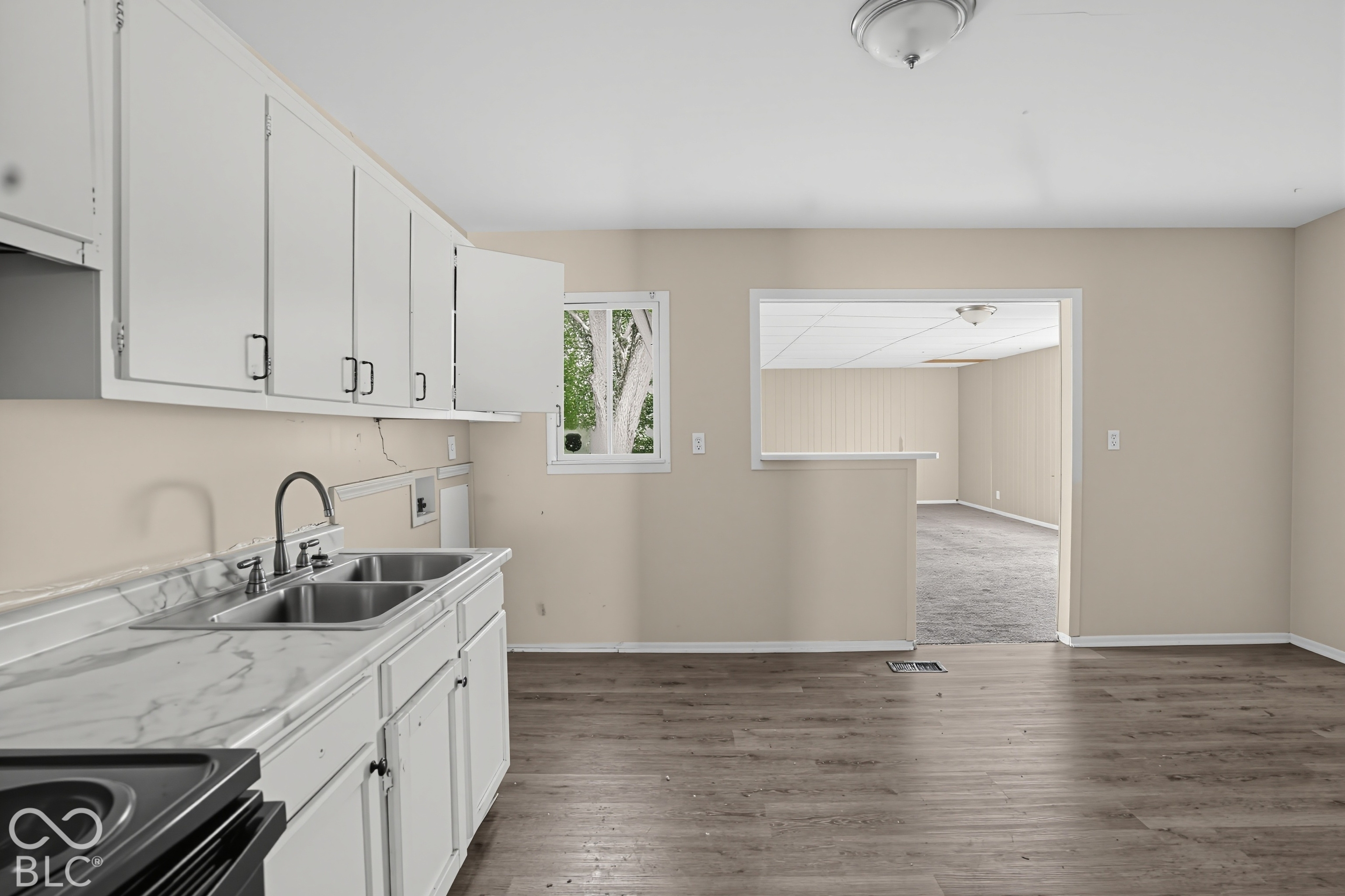 Kitchen featuring white cabinetry, stone-finish countertops, stainless steel dual-basin sink with high-arc faucet, and wood-finish flooring