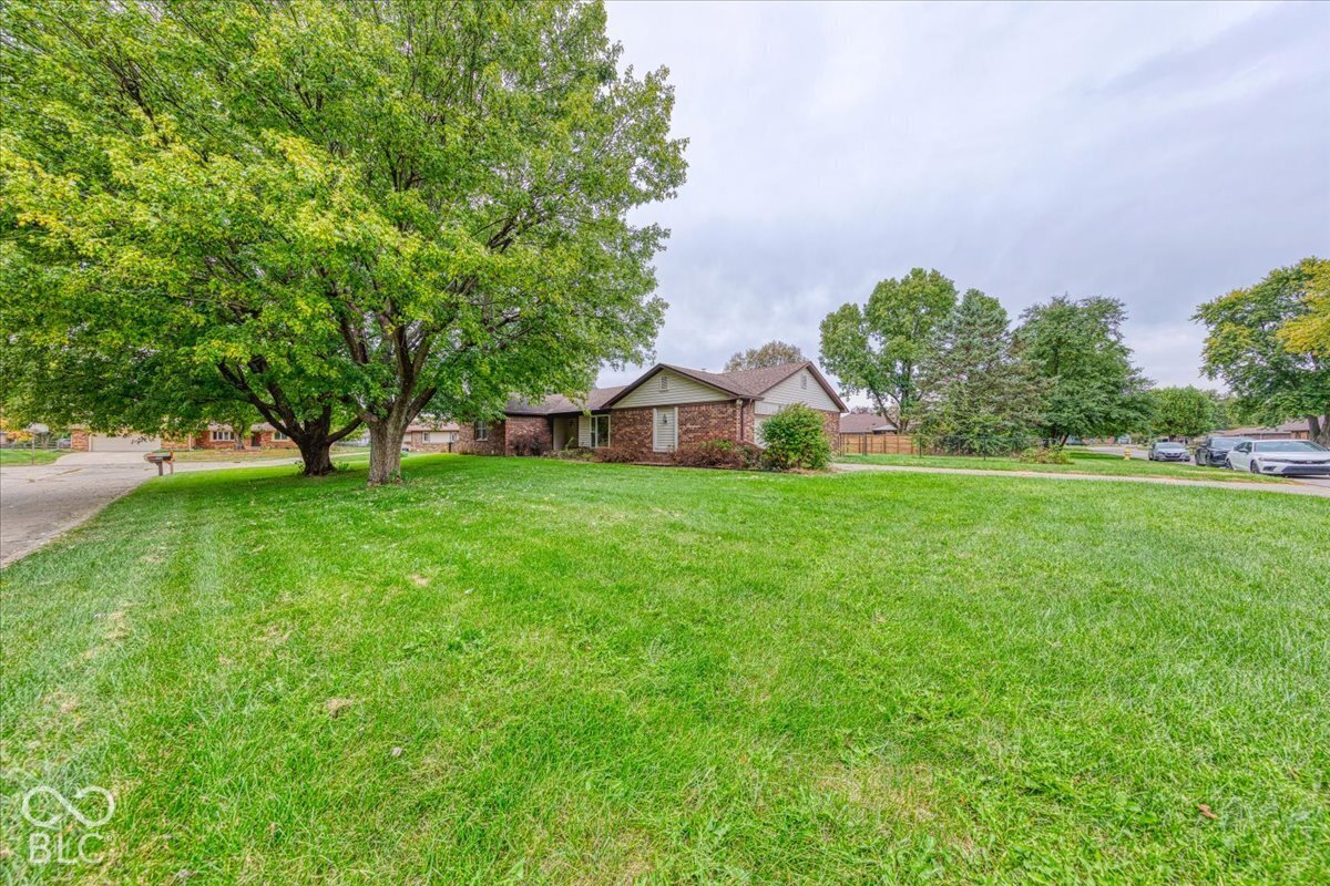 Single-story brick exterior featuring a pitched shingle roof, concrete driveway, and expansive lawn with mature deciduous trees