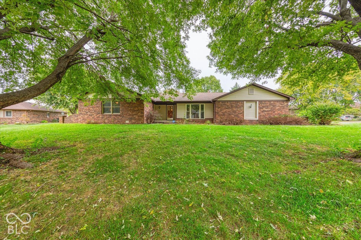 Single-story ranch exterior featuring a brick facade, horizontal siding, asphalt shingle roof, and mature trees on a level lot