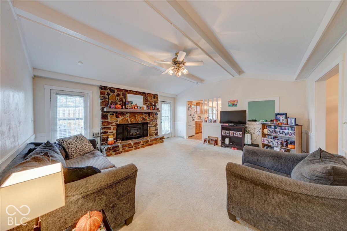 Living area featuring a vaulted ceiling with exposed beams, a floor-to-ceiling stone fireplace, and a ceiling fan