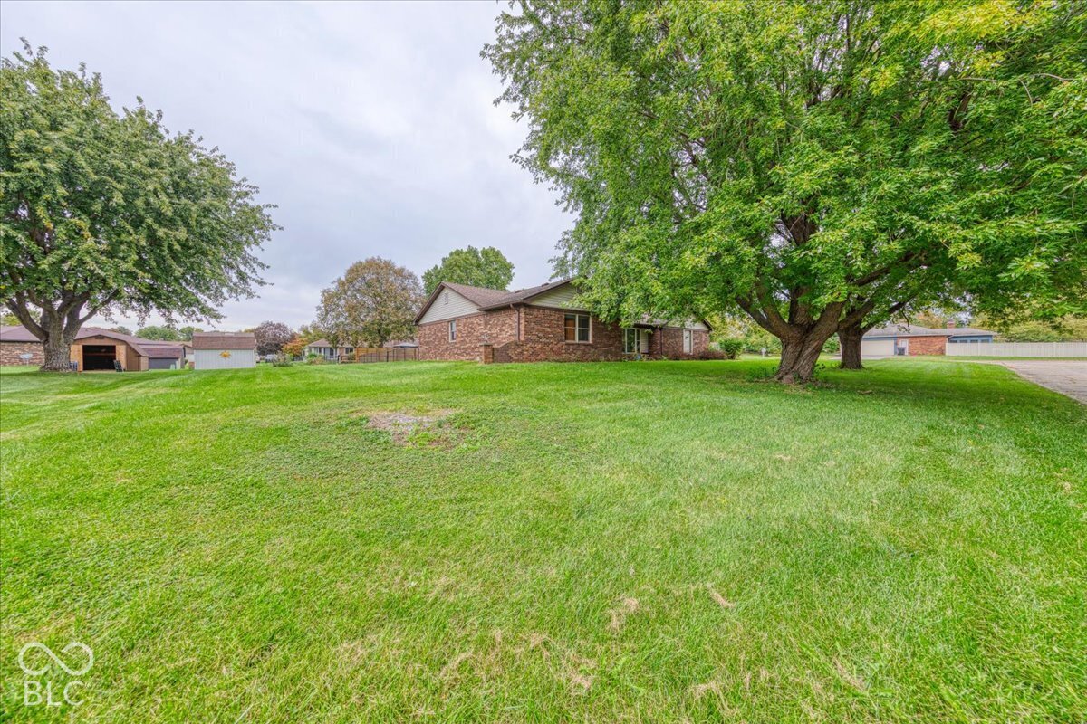 Ranch-style residence featuring a multi-tonal brick exterior, expansive green space, and mature trees on a level lot
