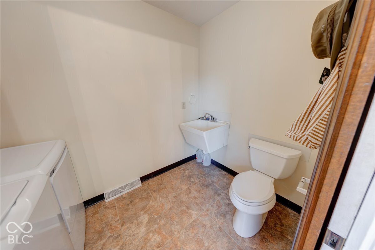 Utility space featuring a wall-mounted basin, porcelain toilet, and resilient patterned flooring