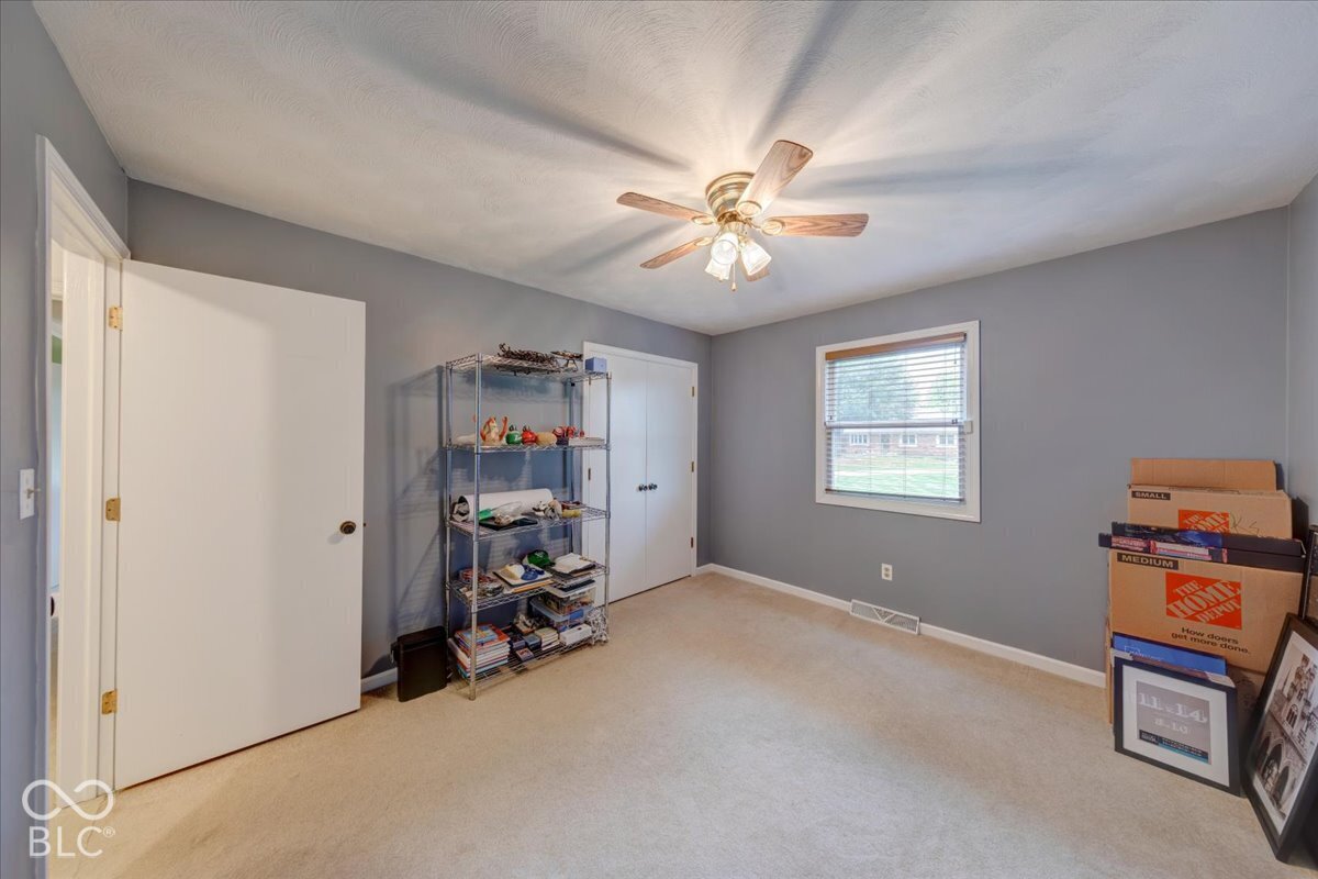 Neutral-toned interior room featuring wall-to-wall carpeting, a multi-blade ceiling fan with integrated lighting, and a double-door closet