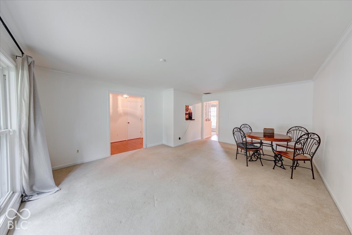 Spacious interior featuring neutral carpeting, white wall finishes, crown molding, and a pass-through wall opening