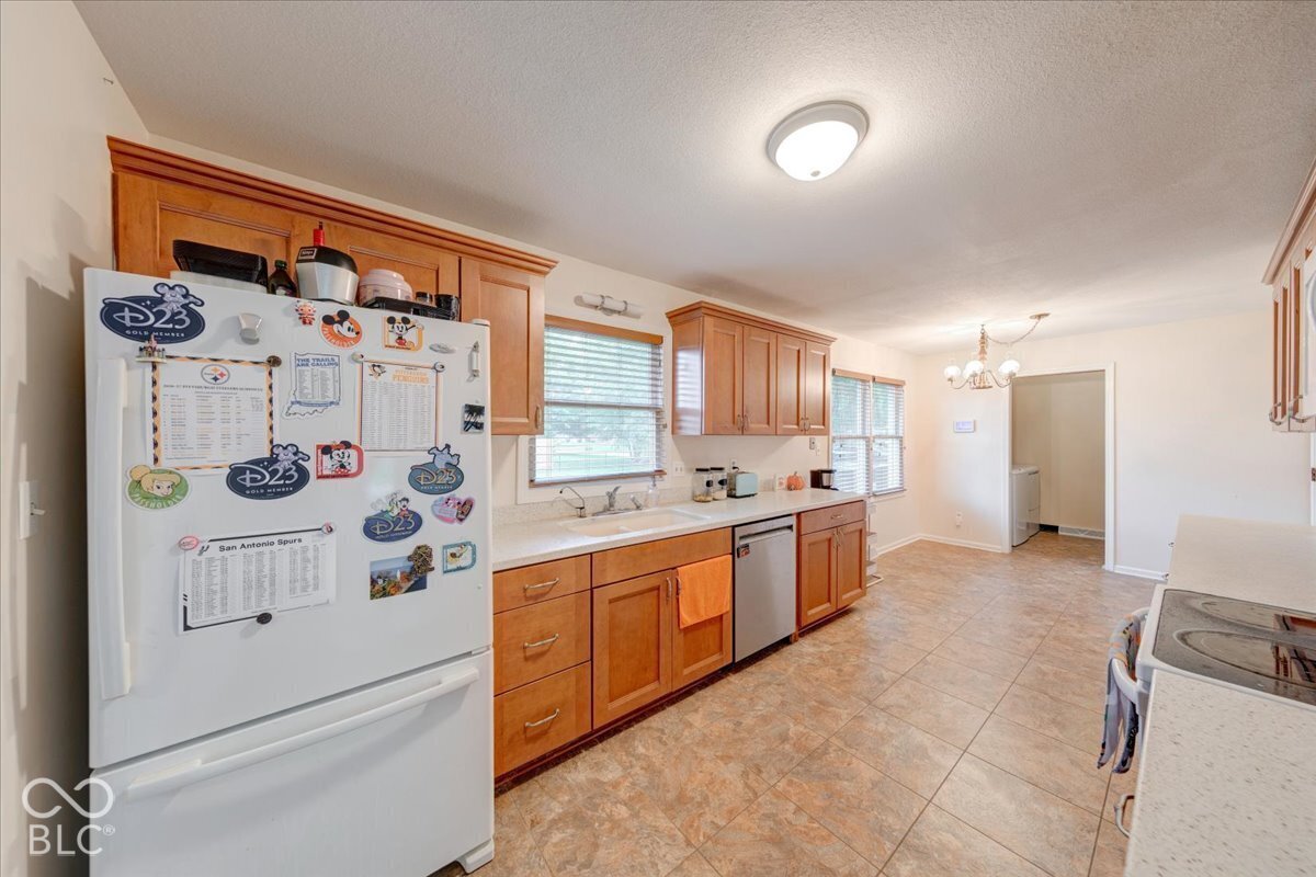 Kitchen featuring solid wood cabinetry, neutral stone-finish countertops, tile flooring, integrated stainless steel dishwasher, and a double-basin sink