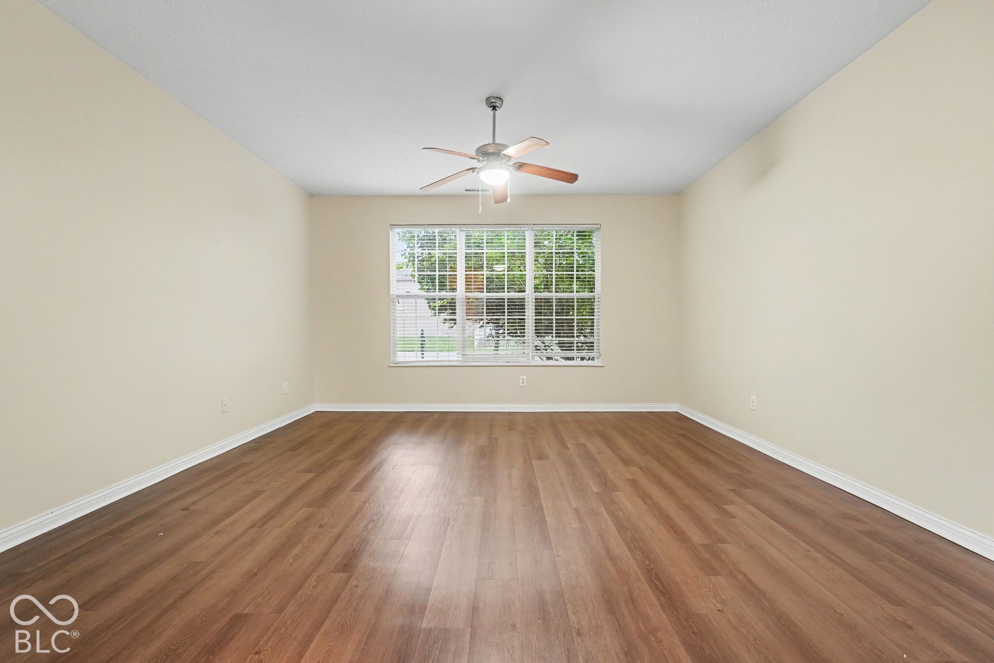 Neutral-toned interior room featuring wood-finish flooring, a multi-pane window, and a central ceiling fan with an integrated light fixture