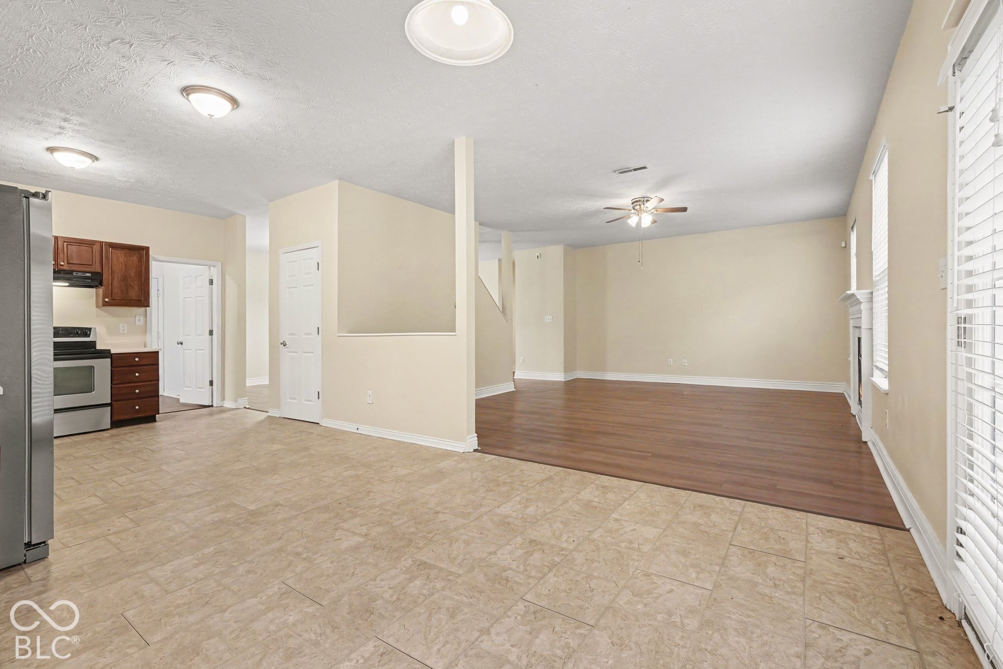 Kitchen featuring wood cabinetry, stainless steel appliances, and ceramic tile flooring, with wood-finish flooring in the living area and an attached fireplace