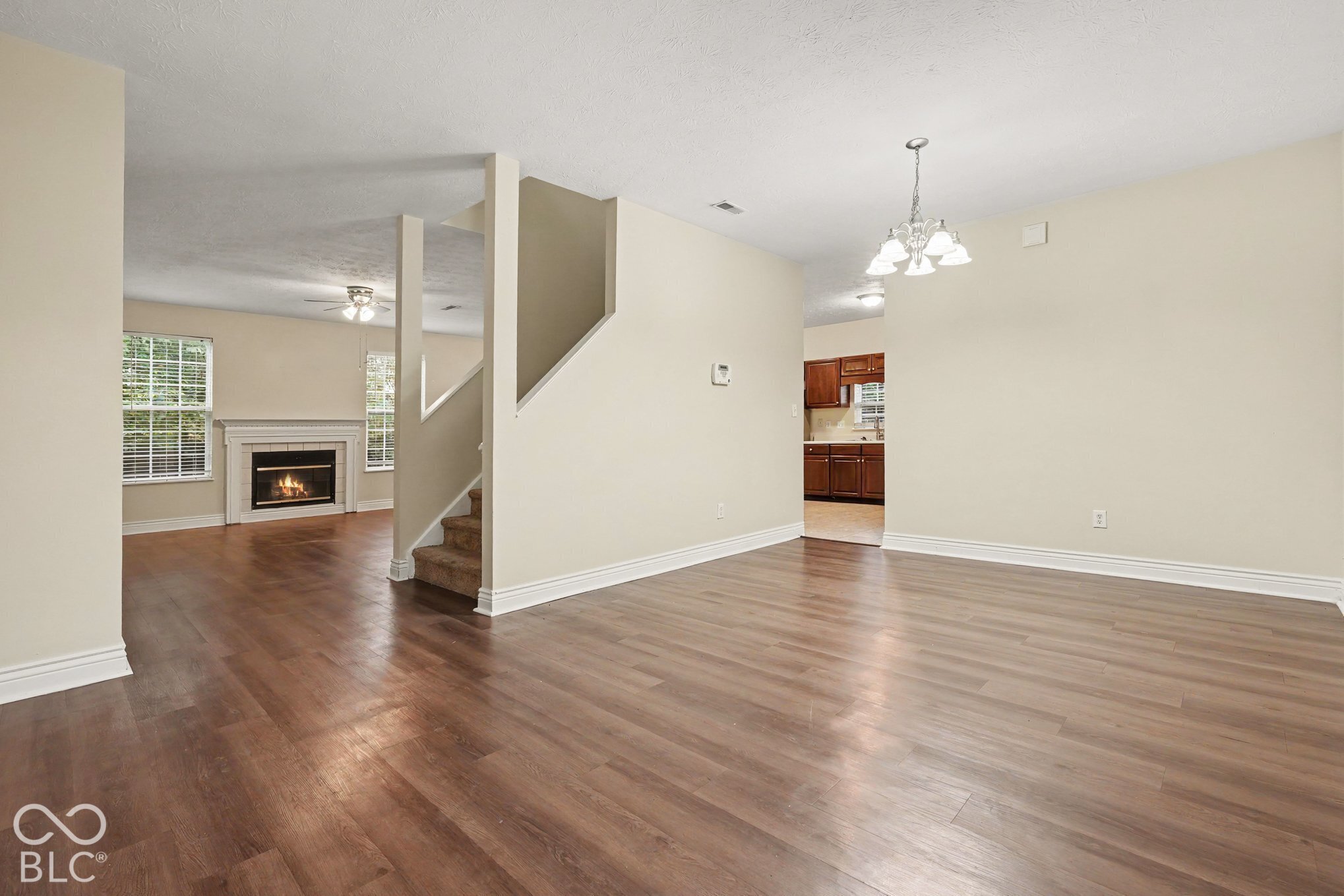 Open-concept interior featuring wood-finish flooring, a fireplace with a mantel, multi-pane windows, a tiered staircase, and a tiered multi-light chandelier
