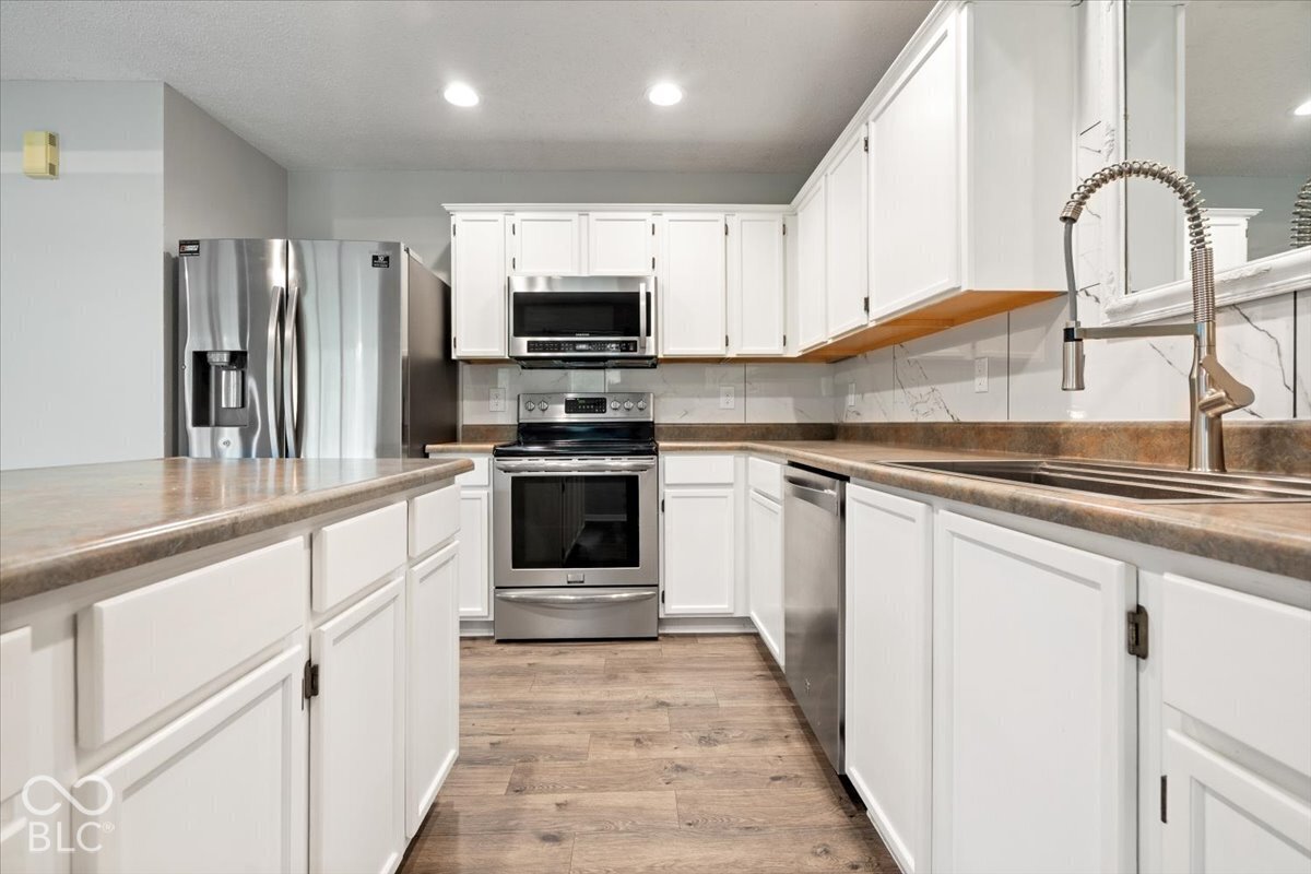 Kitchen featuring white shaker-style cabinetry, stainless steel appliances, stone-patterned backsplash, wood-finish flooring, and a gooseneck pull-down faucet