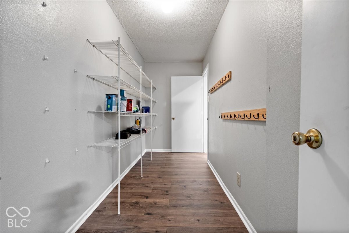 Storage space featuring wood-finish flooring, multi-tier wire shelving, and wall-mounted wooden peg racks