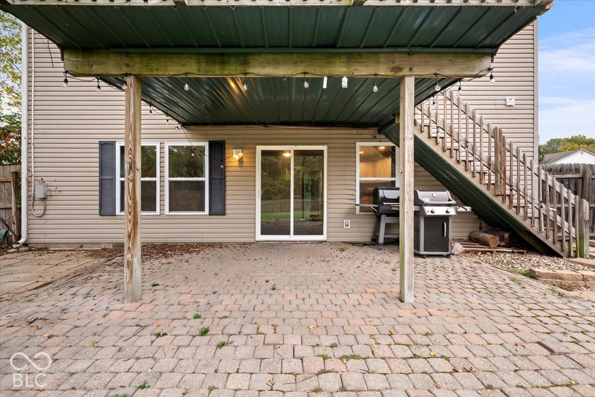 Rear exterior featuring a paver patio, covered porch with metal roofing, sliding glass door, vinyl siding, and exterior wooden staircase