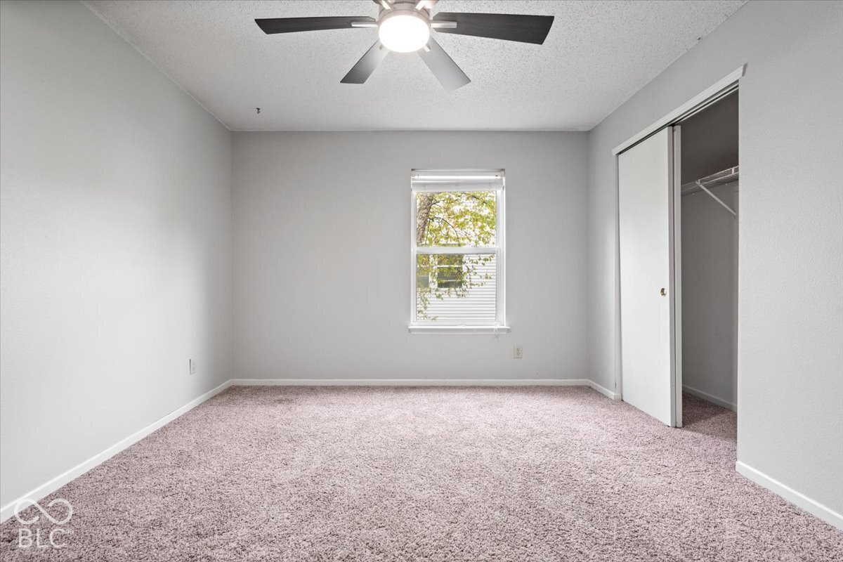 Neutral wall tones, wall-to-wall carpeting, ceiling fan with integrated lighting, window with horizontal blinds, and closet with sliding doors