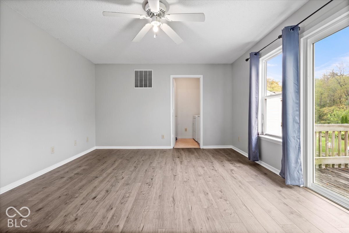 Wood-finish flooring, white ceiling fan with integrated lighting, and glass sliding door featuring exterior wooden decking