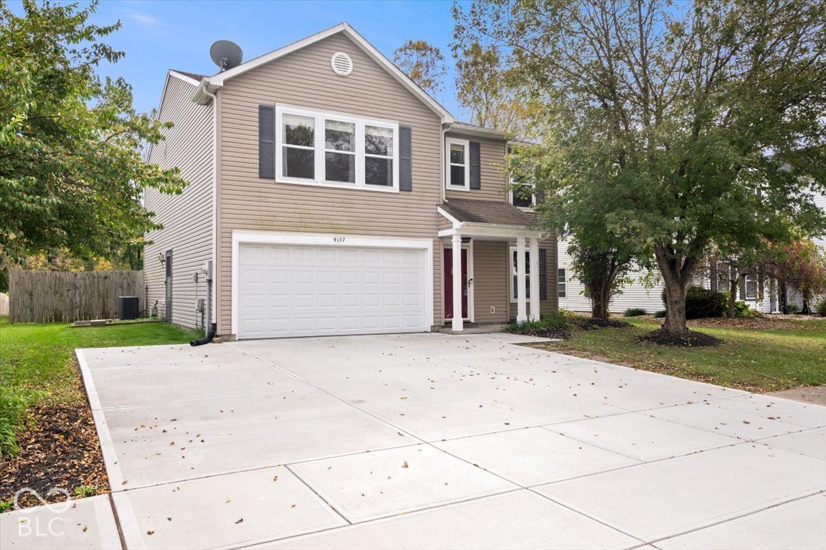 Two-story exterior featuring light-toned horizontal siding, a multi-paneled garage door, shuttered windows, and a covered front entry with columns