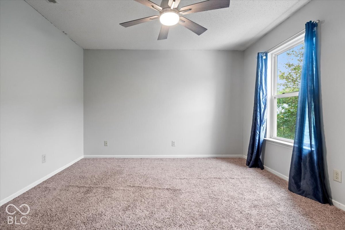 Neutral wall-toned room featuring plush wall-to-wall carpeting, a multi-blade ceiling fan with integrated lighting, and a single-pane window