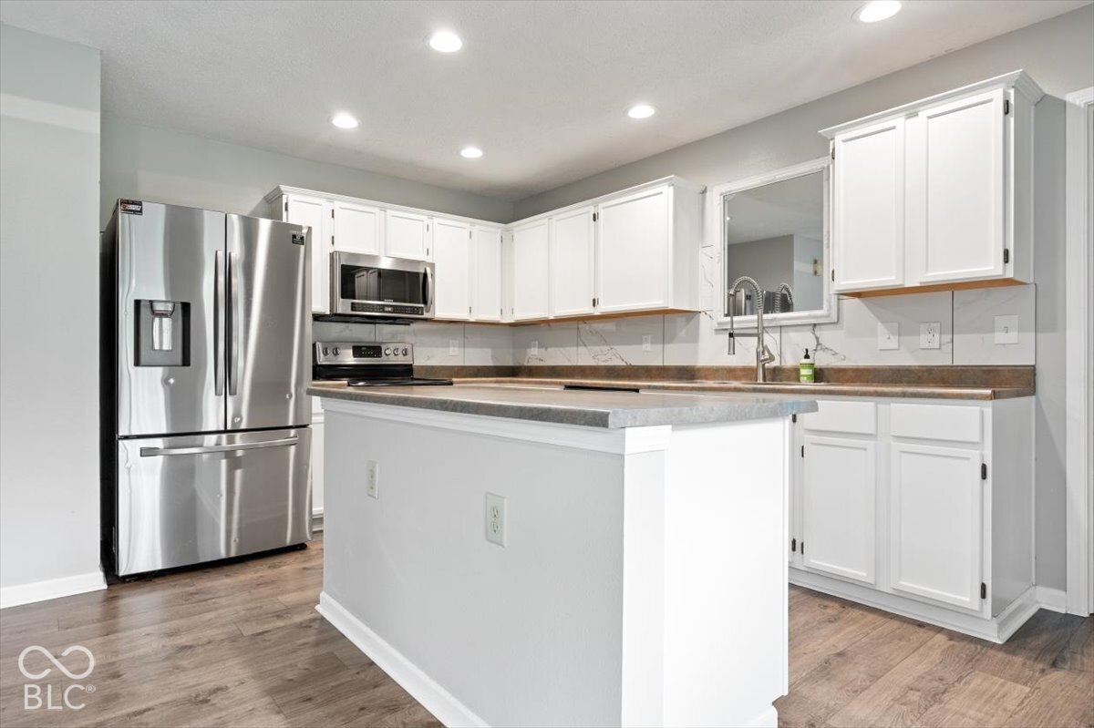 Kitchen featuring white cabinetry, stainless steel appliances, stone-patterned backsplash, wood-finish flooring, and a central island with a solid surface countertop