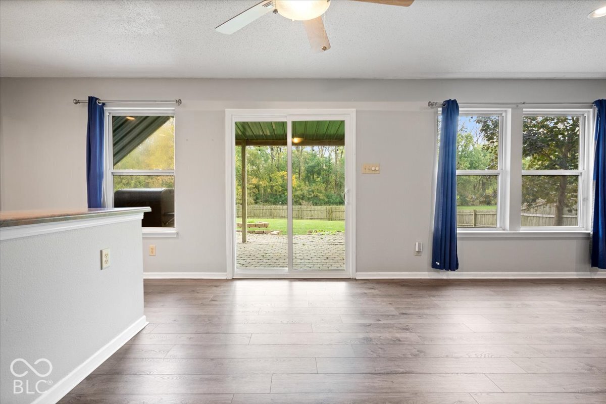 Interior featuring wood-finish flooring, sliding glass door with rear exterior access, three multi-pane windows, and a ceiling-mounted light fixture with fan