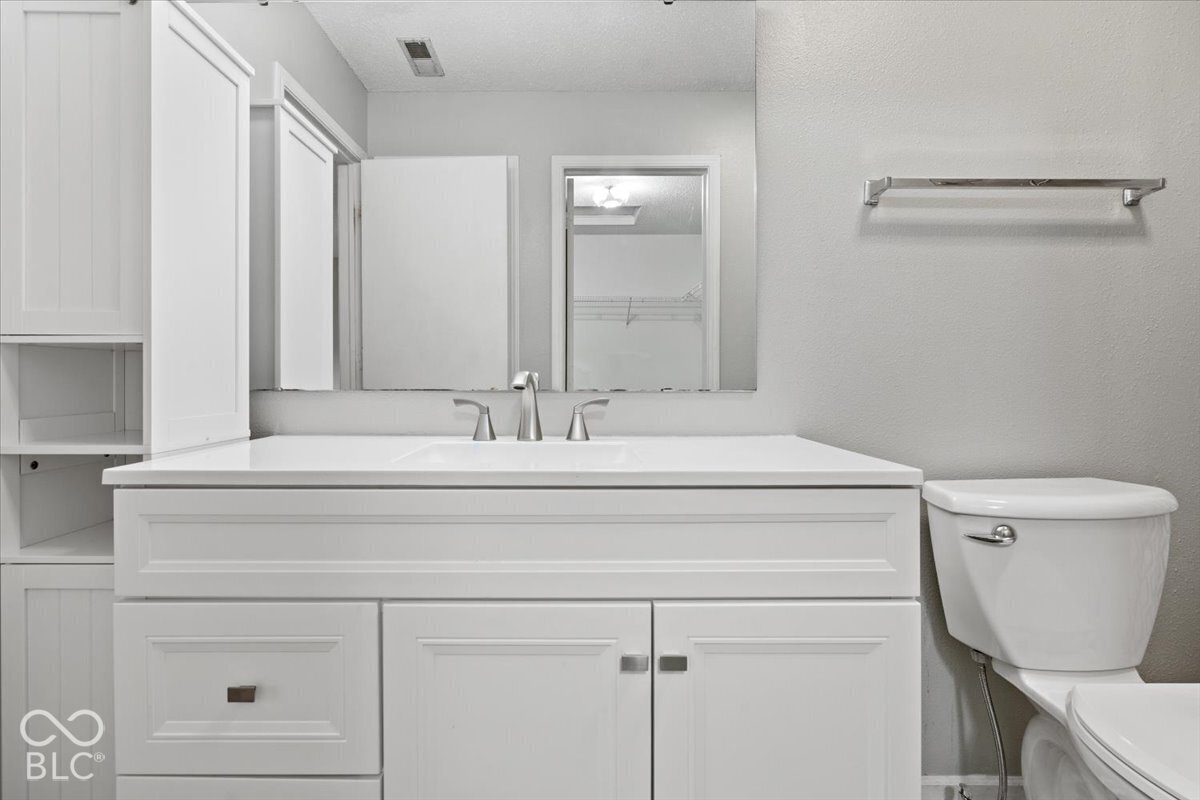 White vanity featuring integrated countertop, Shaker-style cabinetry with built-in side shelving, metallic finish hardware, and wall-to-wall mirror