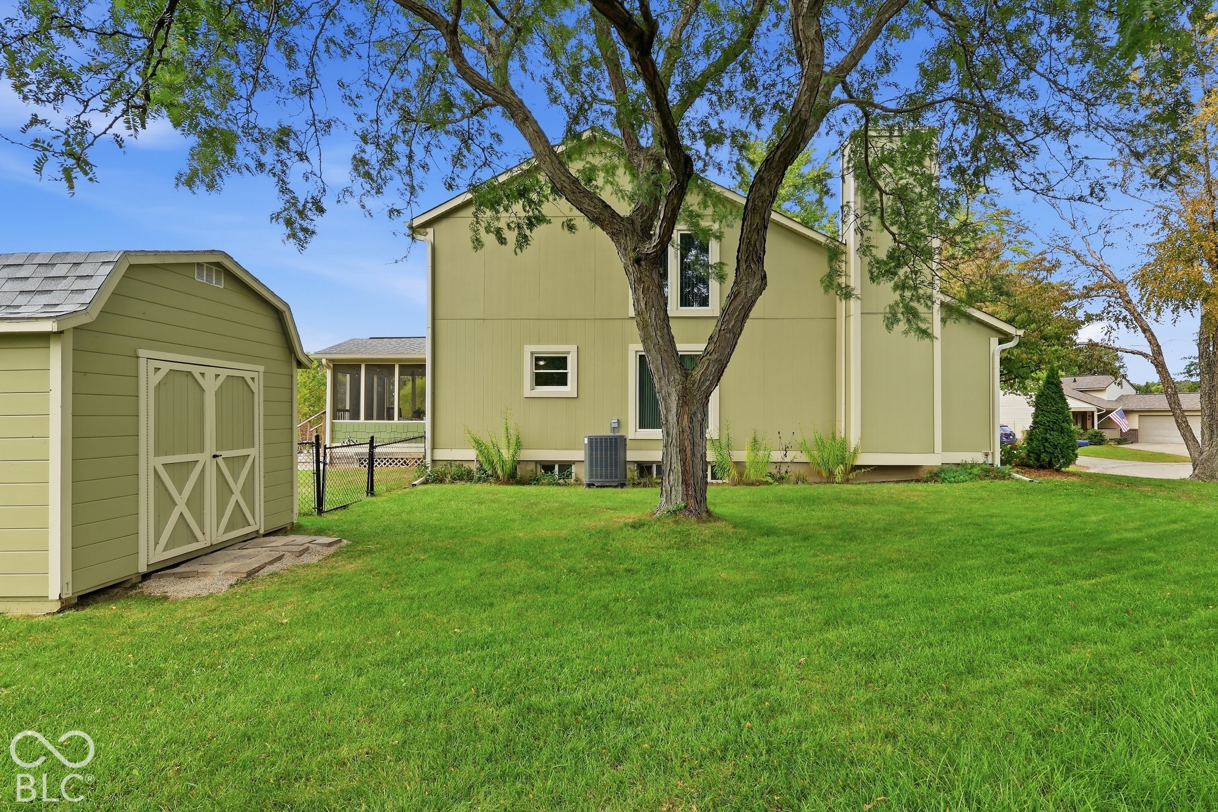 Rear exterior featuring a detached storage shed, exterior chimney, screened-in porch, and expansive lawn with mature trees